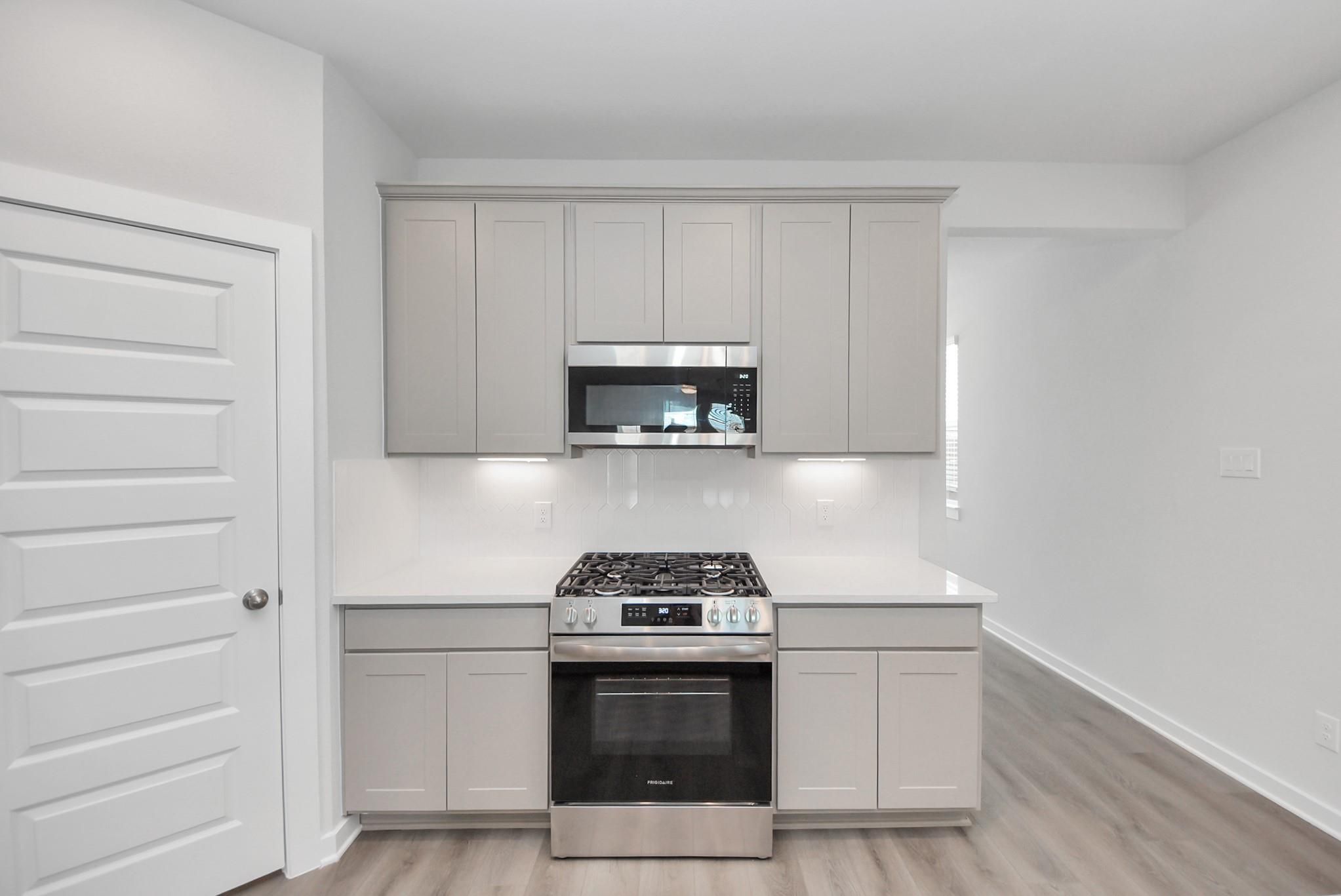 Modern kitchen with gray shaker cabinets, stainless gas range and microwave, white quartz countertops in Davidson Homes The San Marcos E, Beasley, TX