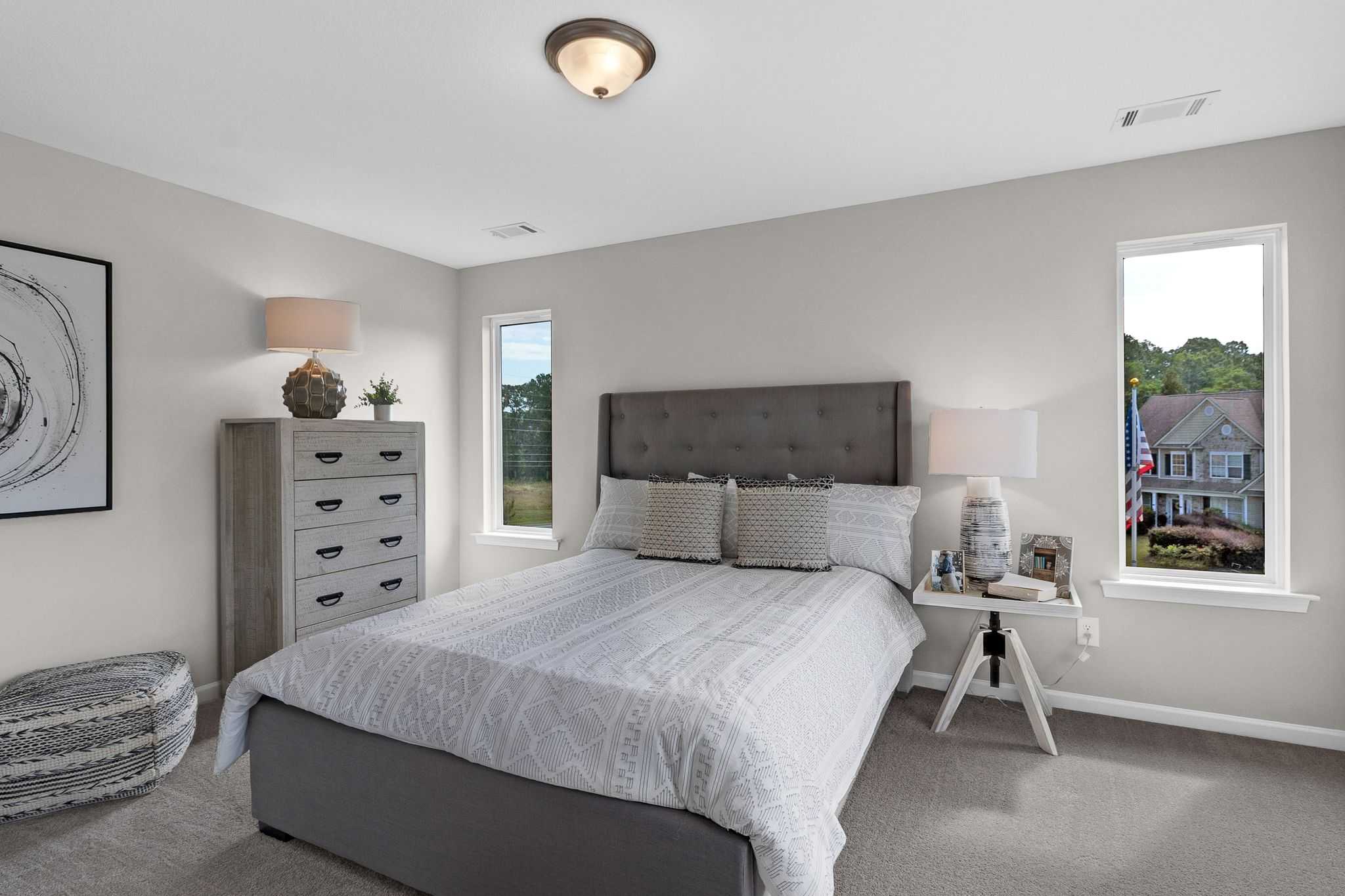 Spacious bedroom in Ivy Glen Perry GA with gray walls tufted headboard white bedding dresser lamps and neighborhood view
