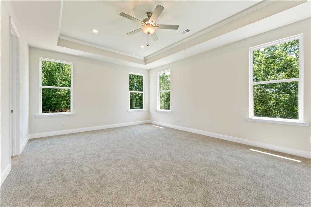 Bright empty bedroom with tray ceiling, ceiling fan, large windows, and tree views in Davidson Homes The Hampton C, Buford, GA