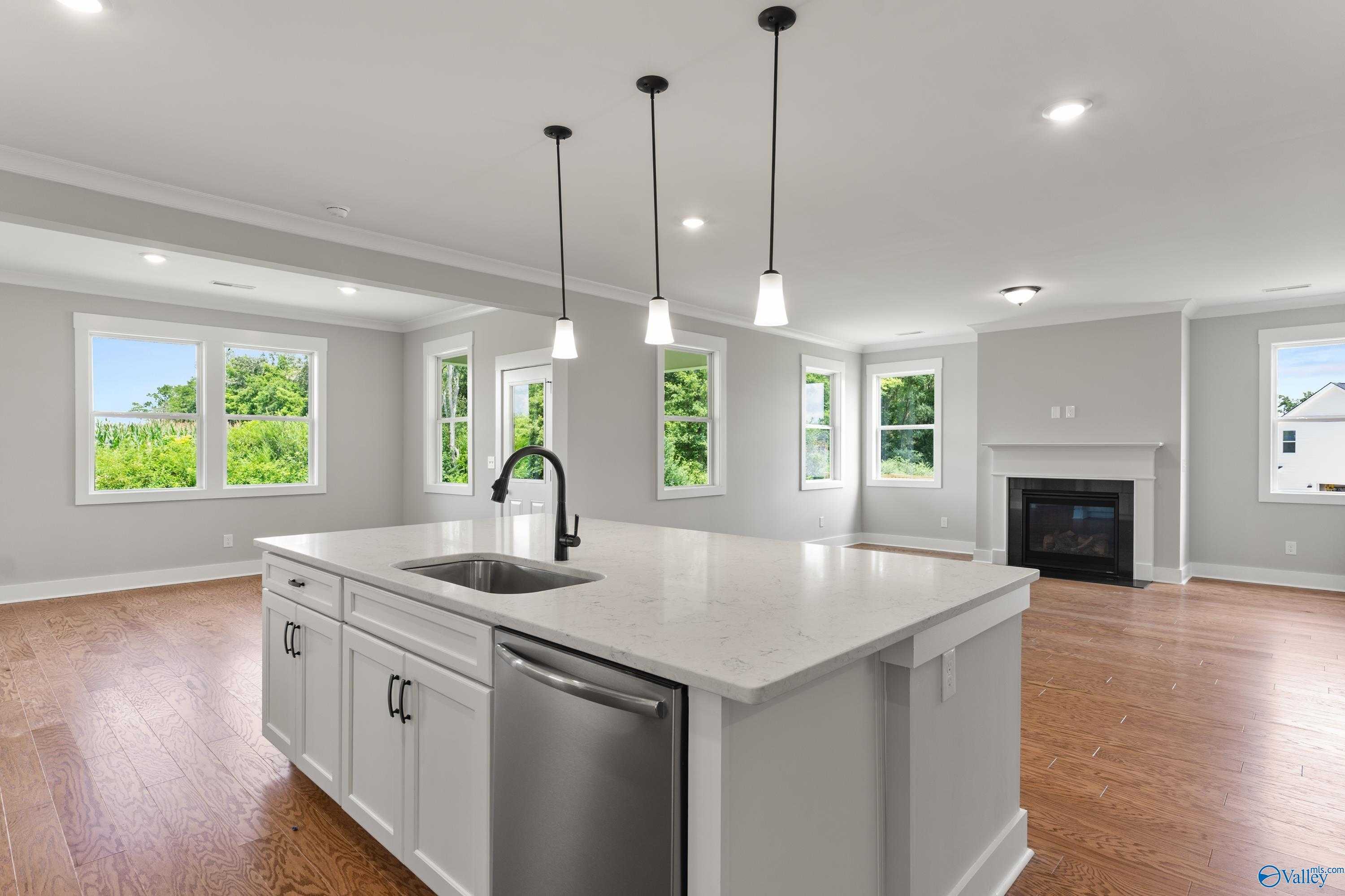 Bright open-concept kitchen with white quartz island, sink, stainless dishwasher, and adjacent living room fireplace in The Arcadia, Huntsville AL