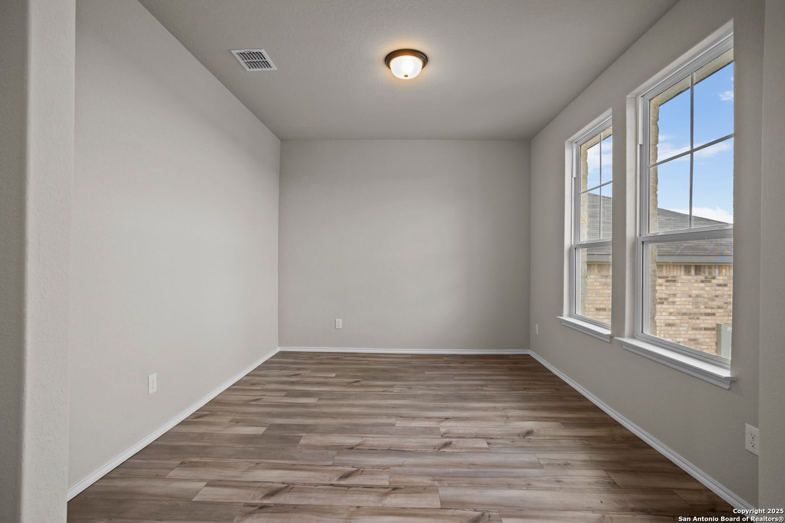 Bright empty bedroom with light gray walls, hardwood floors, and large windows in Davidson Homes The Douglas F, San Antonio