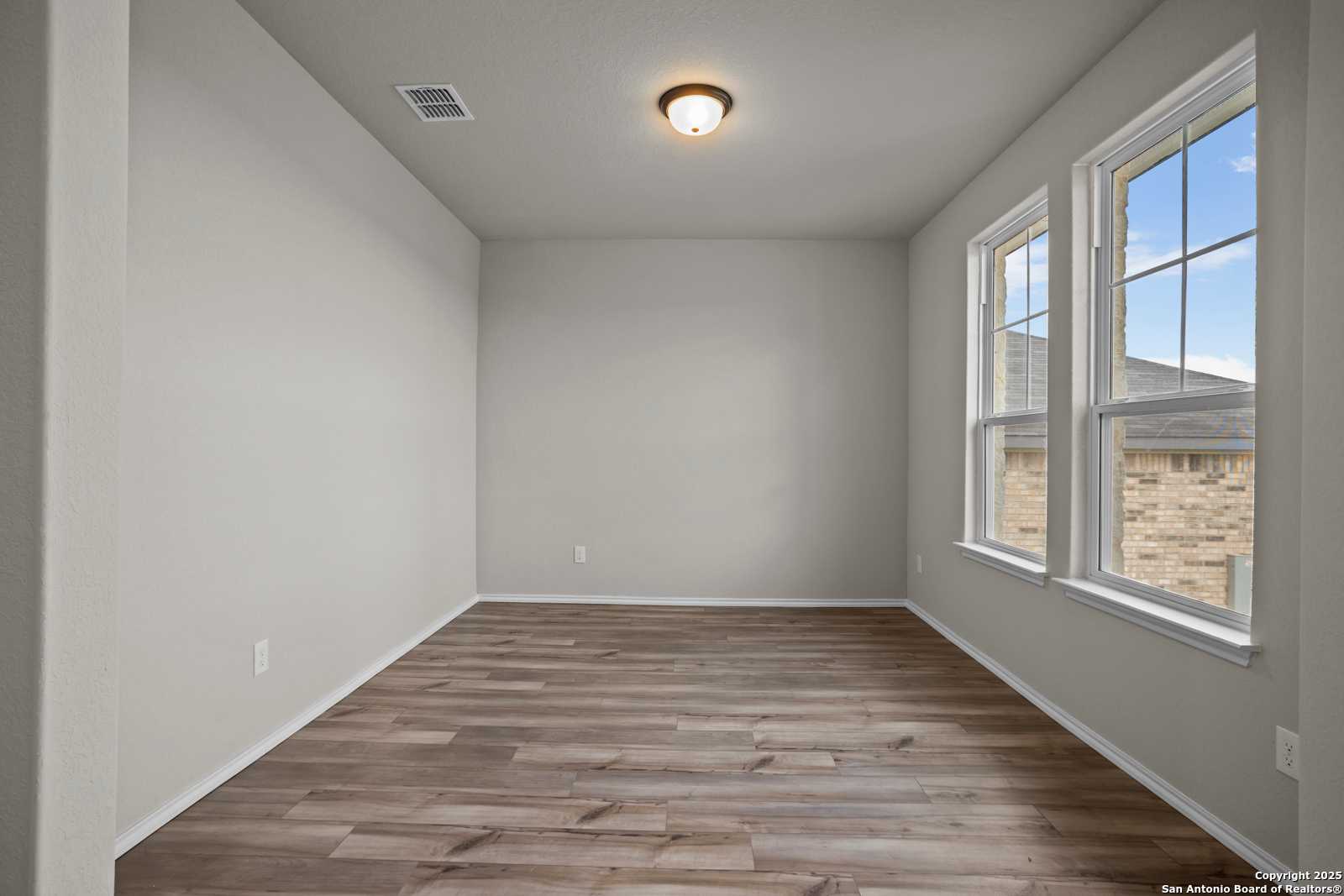 Bright empty bedroom with light gray walls, hardwood floors, and large windows in Davidson Homes The Douglas F, San Antonio