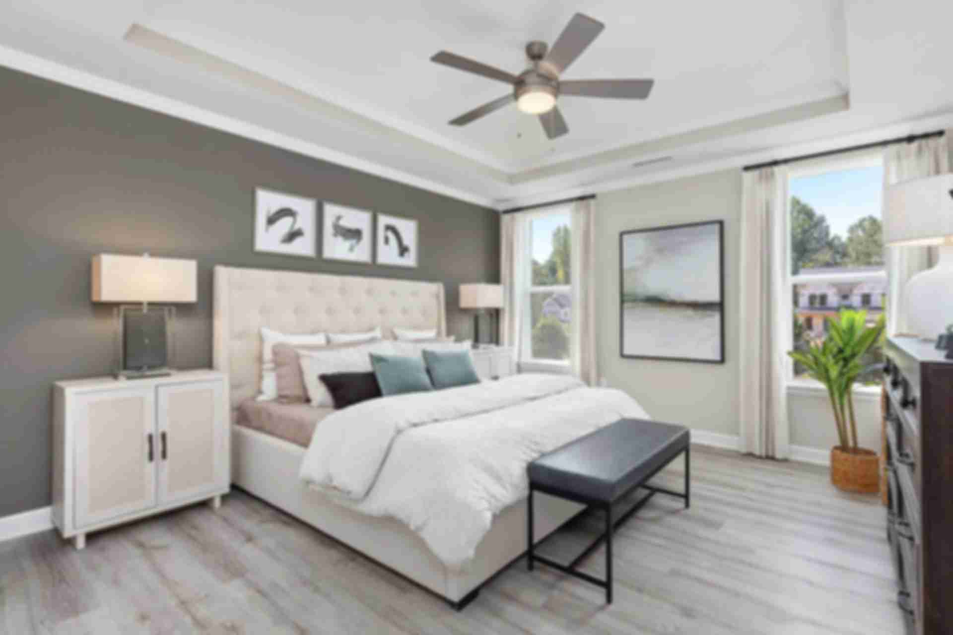 Spacious primary bedroom at Prince Place in Fuquay-Varina NC with king bed, gray accent wall, ceiling fan, and large window views