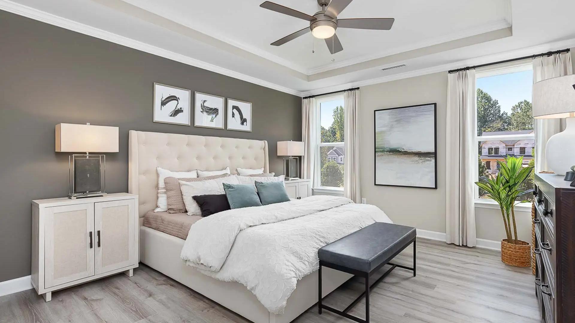 Spacious primary bedroom at Prince Place in Fuquay-Varina NC with king bed, gray accent wall, ceiling fan, and large window views