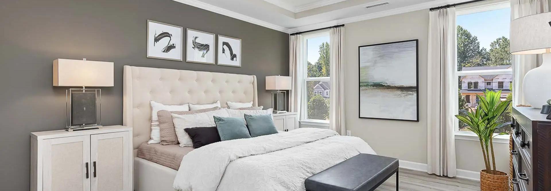 Spacious primary bedroom at Prince Place in Fuquay-Varina NC with king bed, gray accent wall, ceiling fan, and large window views