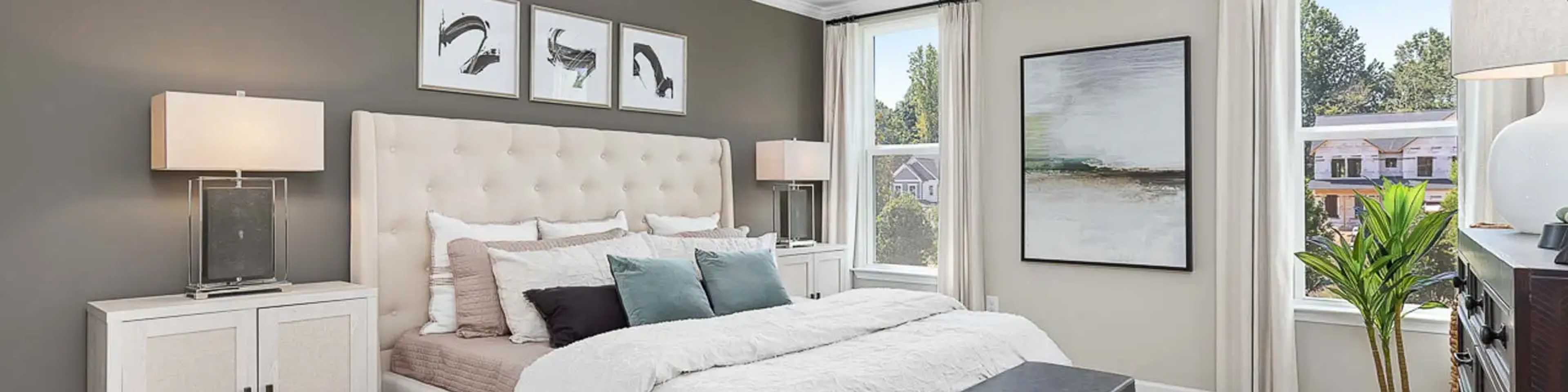 Spacious primary bedroom at Prince Place in Fuquay-Varina NC with king bed, gray accent wall, ceiling fan, and large window views