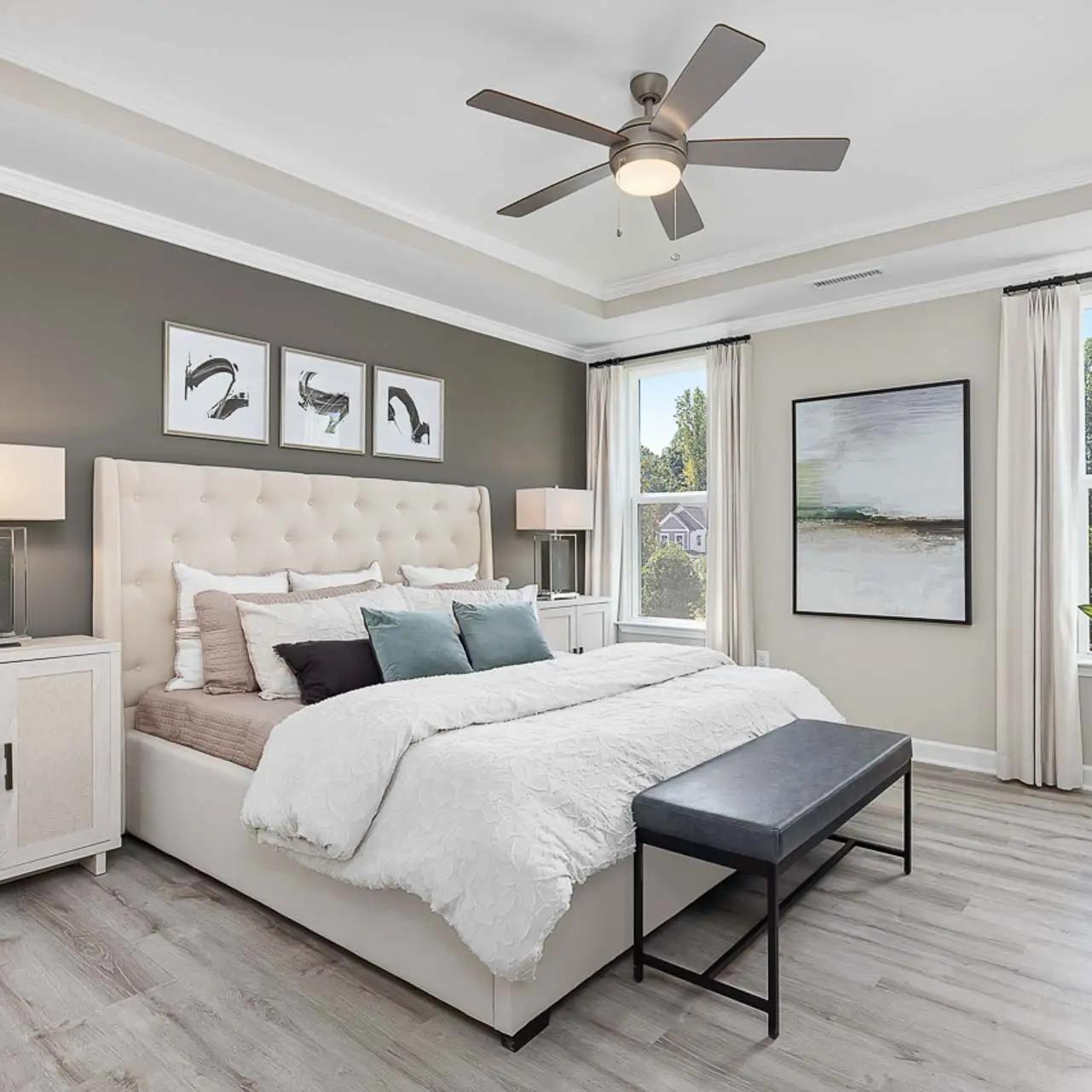 Spacious primary bedroom at Prince Place in Fuquay-Varina NC with king bed, gray accent wall, ceiling fan, and large window views
