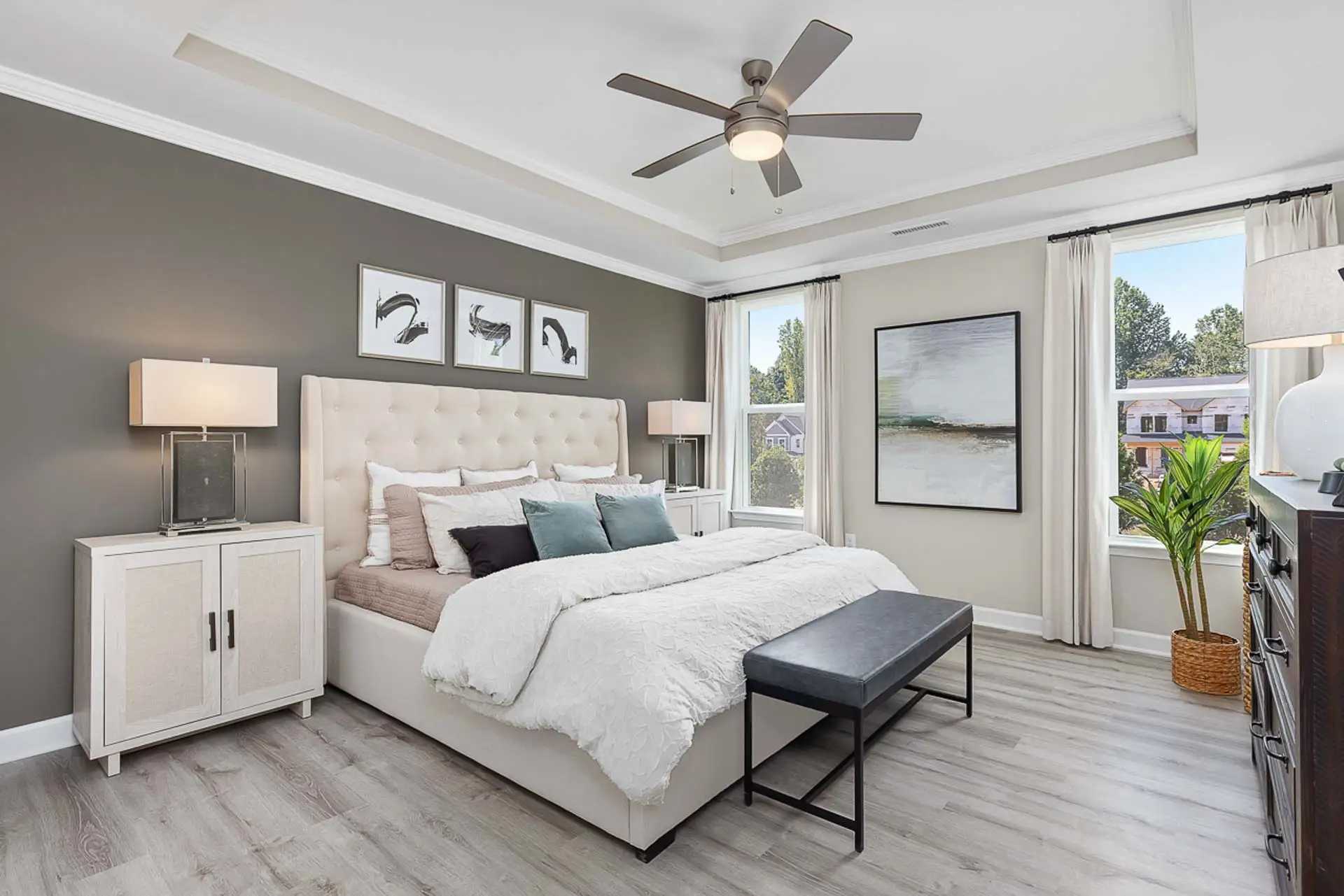 Spacious primary bedroom at Prince Place in Fuquay-Varina NC with king bed, gray accent wall, ceiling fan, and large window views