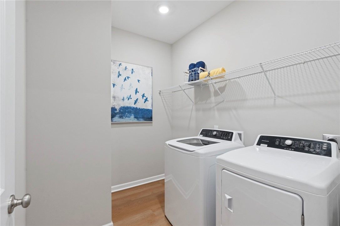 Modern laundry room with white front-load washer dryer, wire shelves holding blue towels, abstract blue art on gray walls in The Phoenix B home, Opelika