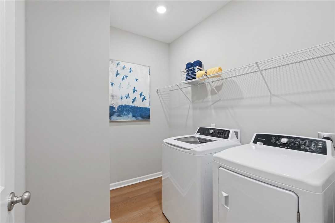 Modern laundry room with white front-load washer dryer, wire shelves holding blue towels, abstract blue art on gray walls in The Phoenix B home, Opelika