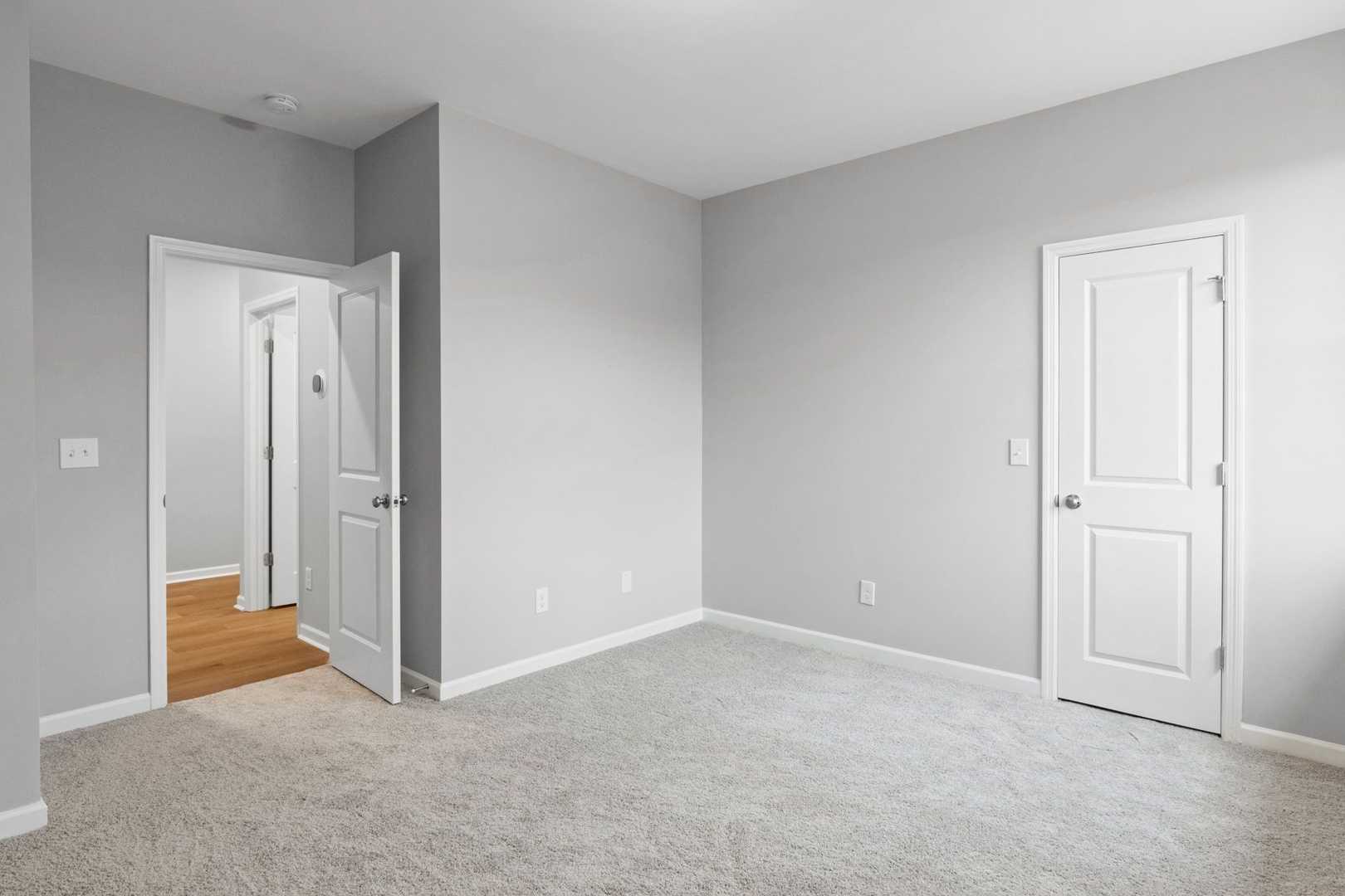 Spacious bedroom interior in The Luna home by Evermore Homes, Perry GA, featuring gray walls, carpet floor, and bath doorway