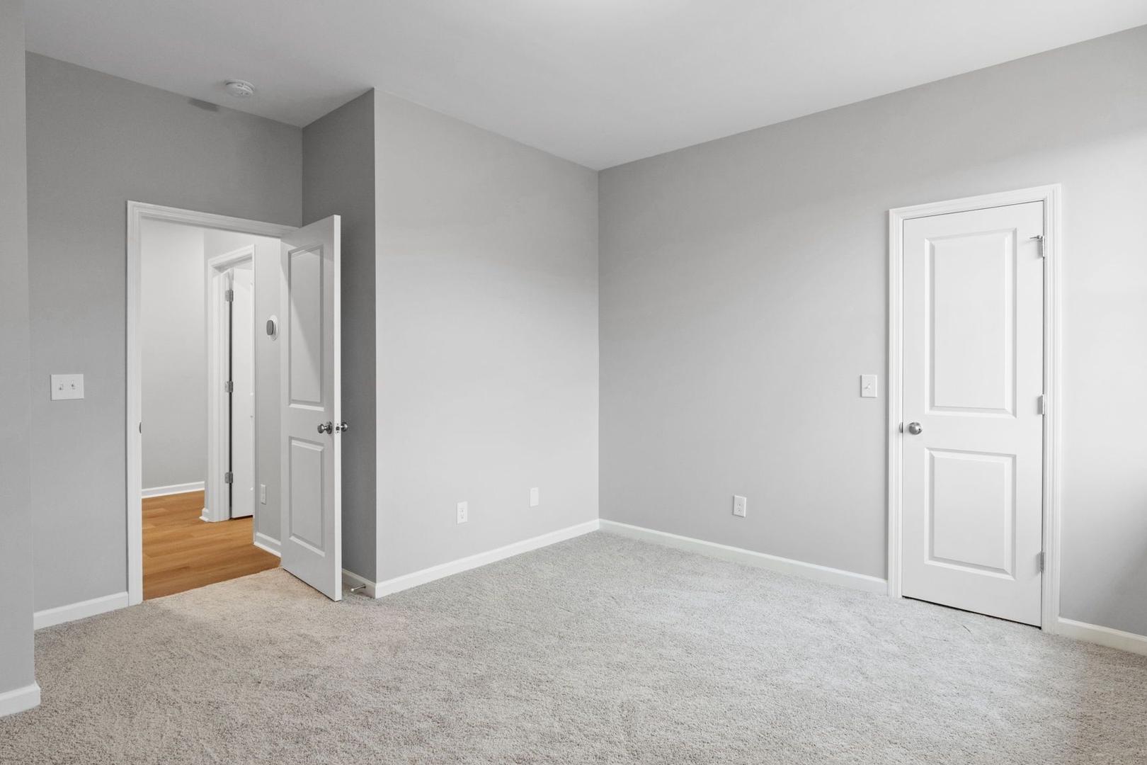Spacious bedroom interior in The Luna home by Evermore Homes, Perry GA, featuring gray walls, carpet floor, and bath doorway