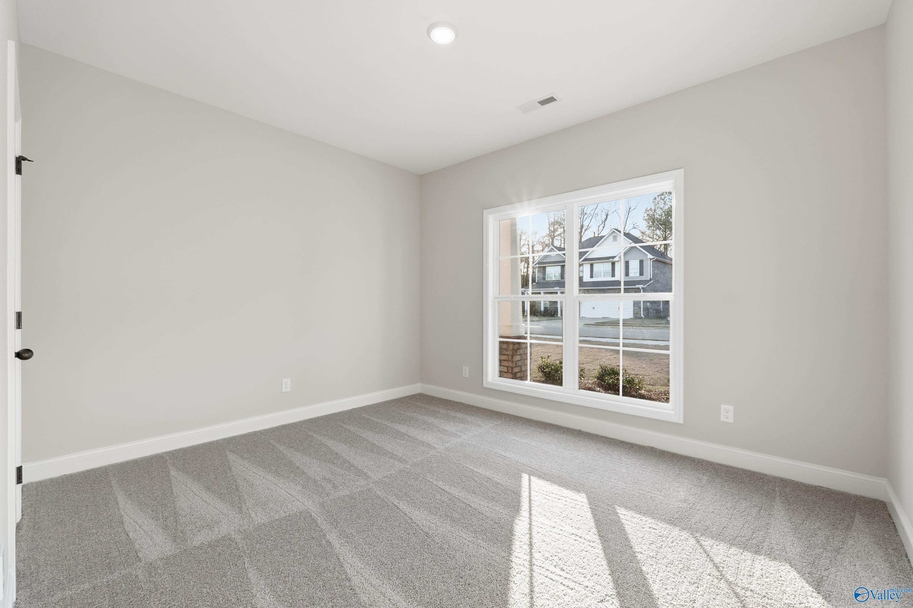 Sunlit empty bedroom with gray walls, beige carpet, and large window view in Davidson Homes The Daphne D, Arab, Alabama