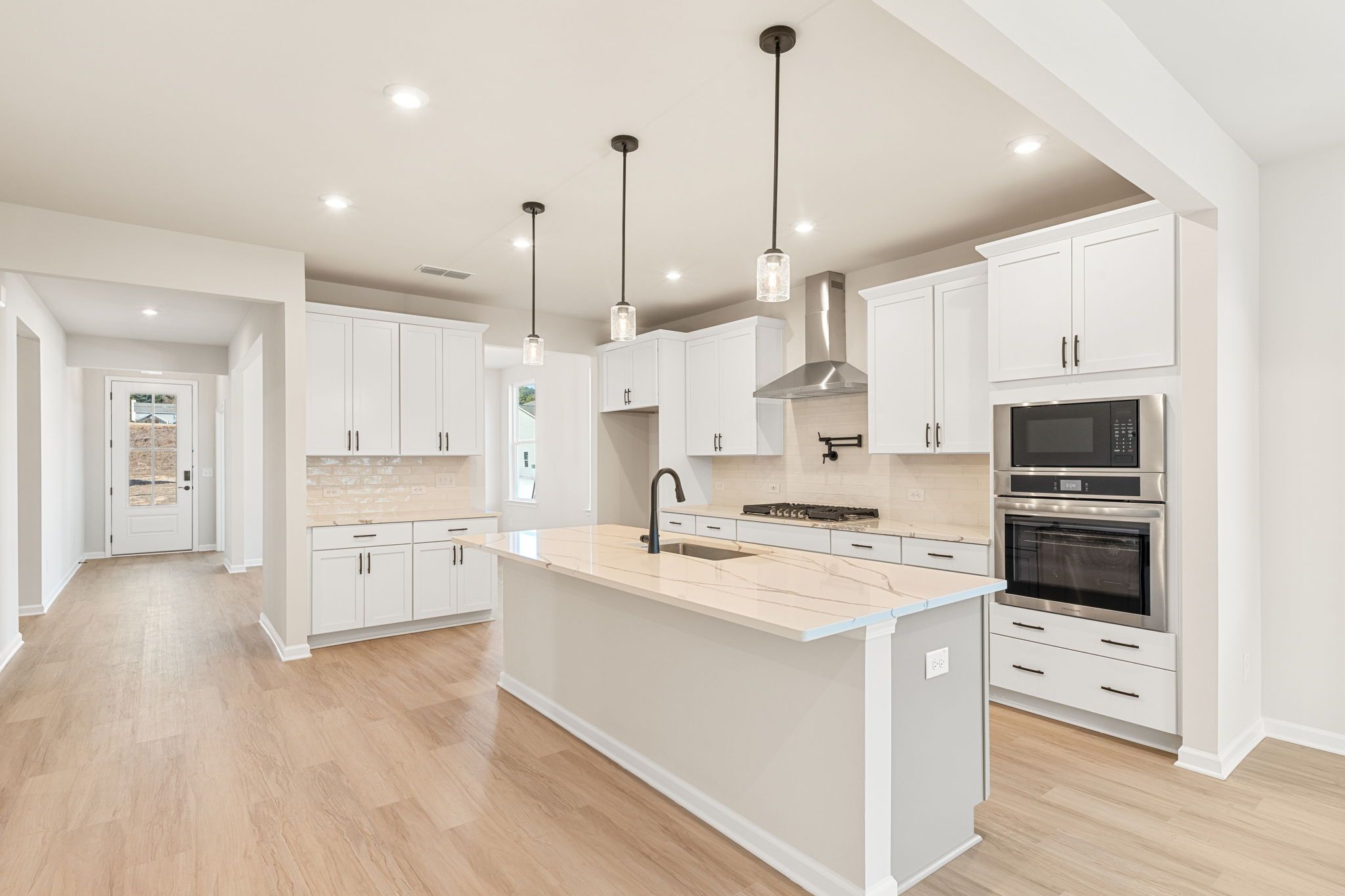 Modern white kitchen with quartz island, stainless double oven, subway backsplash, and hardwood floors in The Glenwood C, Loganville, GA