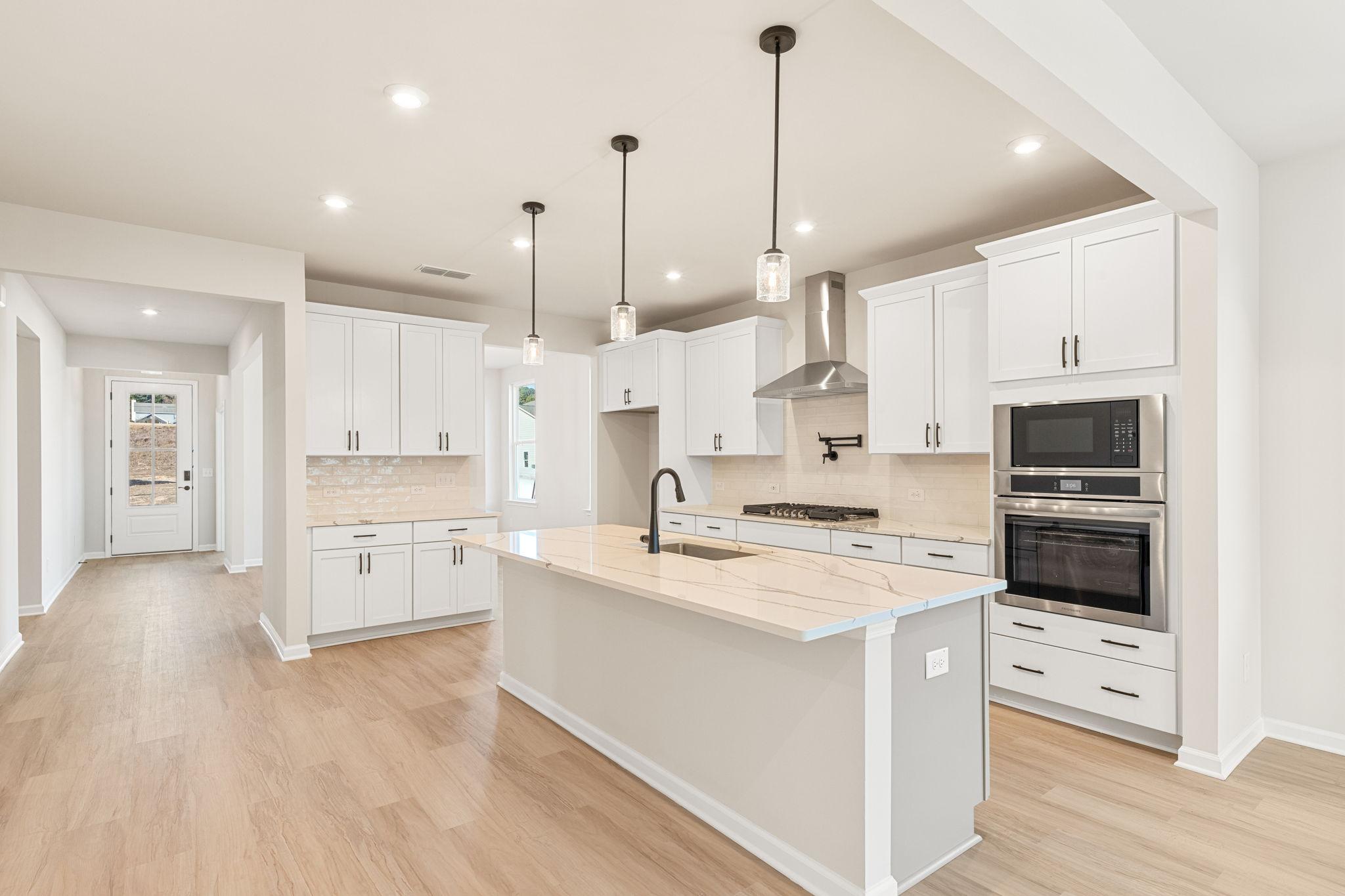 Modern white kitchen with quartz island, stainless double oven, subway backsplash, and hardwood floors in The Glenwood C, Loganville, GA