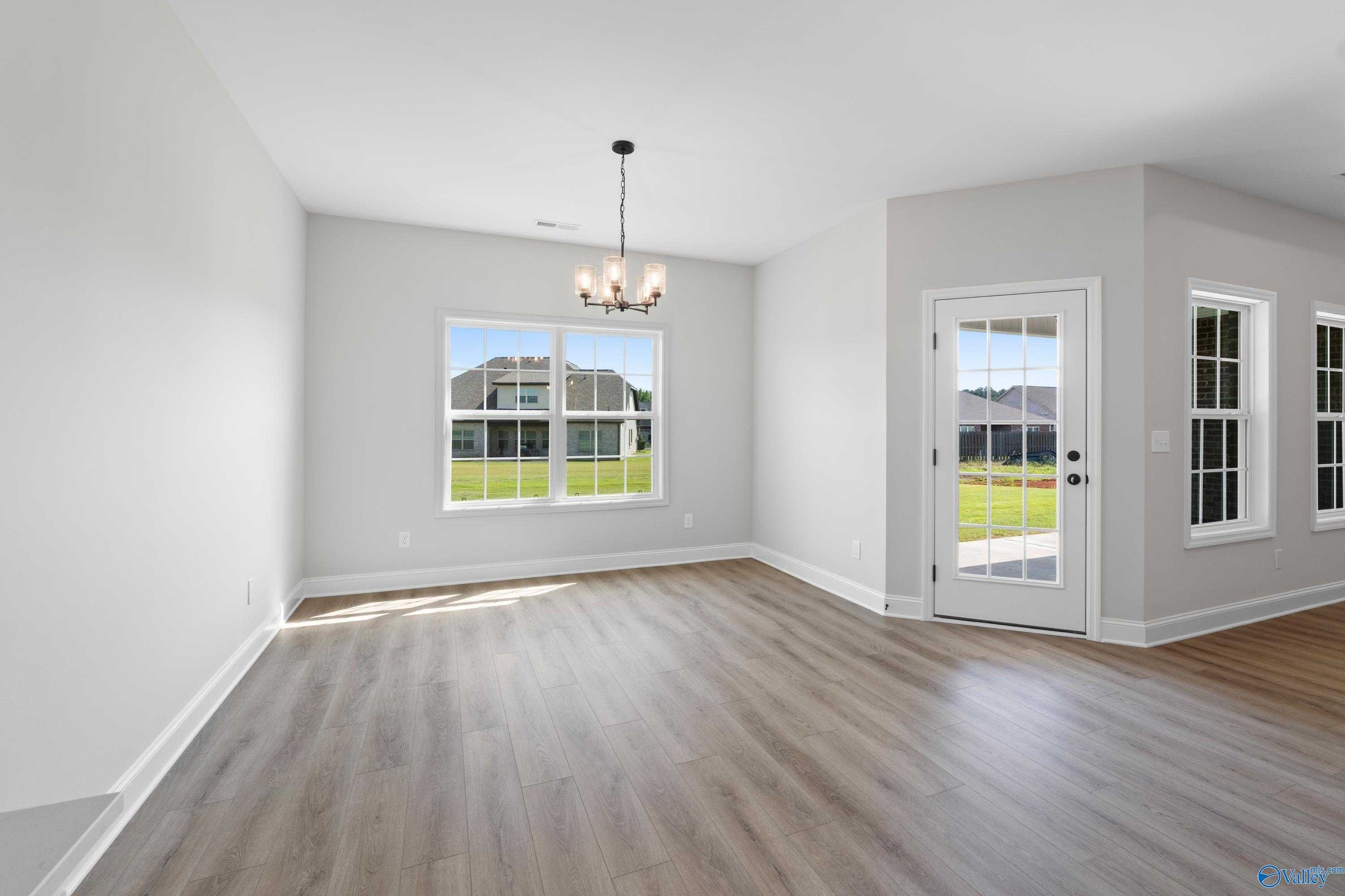 Bright living room with hardwood floors, chandelier, large windows overlooking green lawn, and French door to patio in The Rockford floor plan, Toney, Alabama