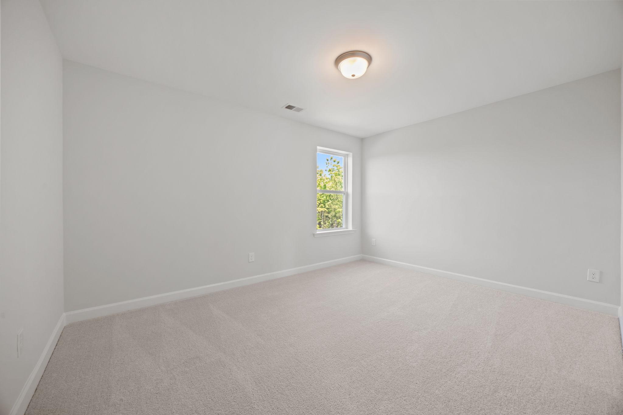 Spacious, light-filled secondary bedroom in The Ashport B floor plan featuring neutral paint and plush carpeting.