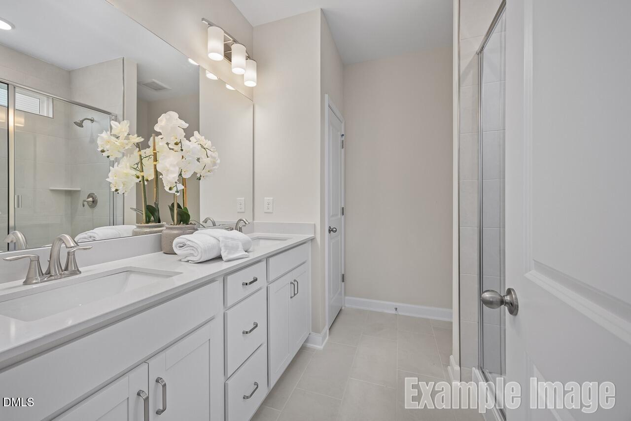 Elegant master bathroom with double vanity, white shaker cabinets, orchids, and glass shower in Davidson Homes The Carter C, Lillington, NC