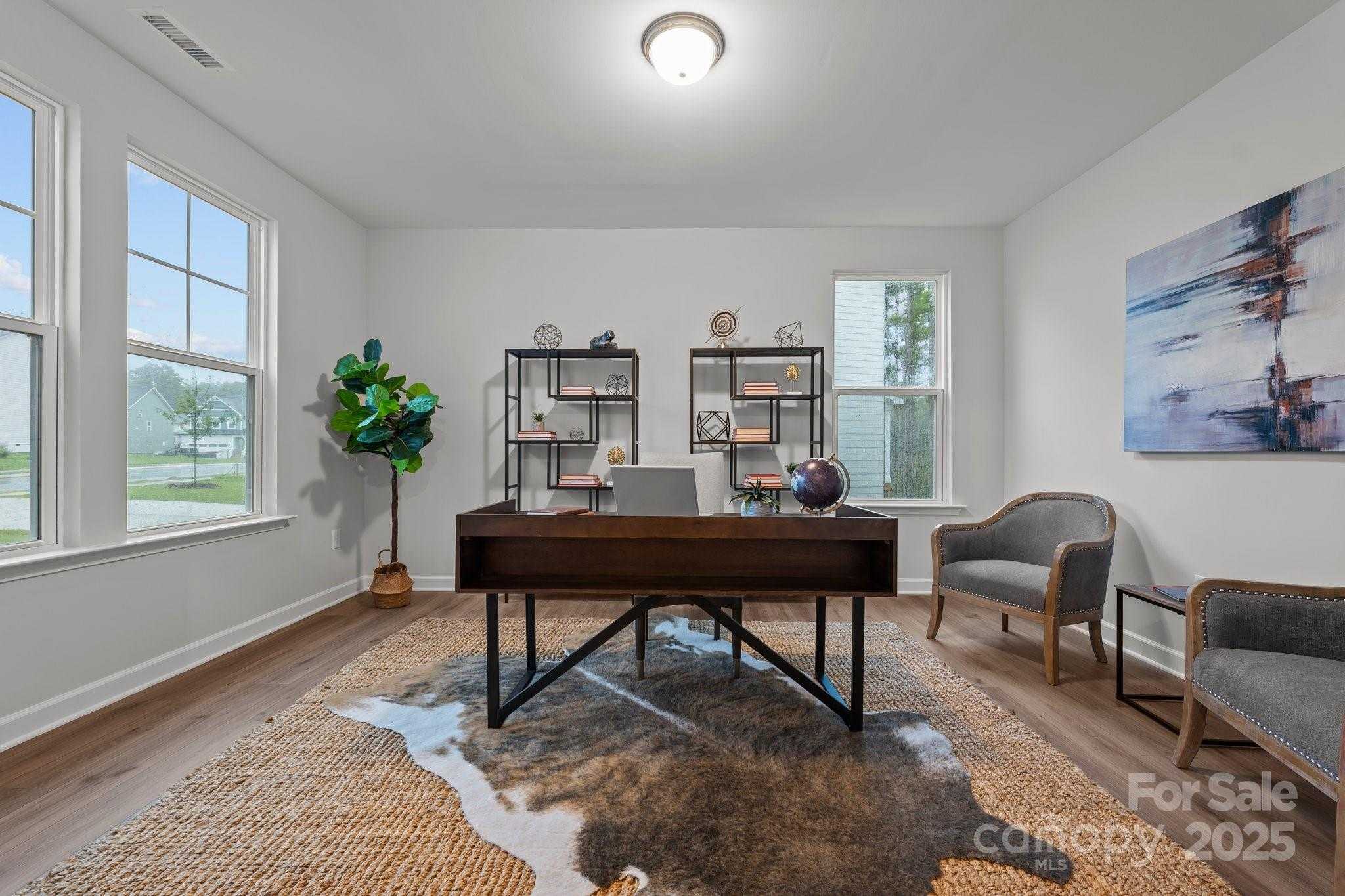 Modern home office with wooden desk, metal shelves, fiddle leaf plant, abstract art, and large windows in Davidson Homes The Hickory E II, Belmont, NC
