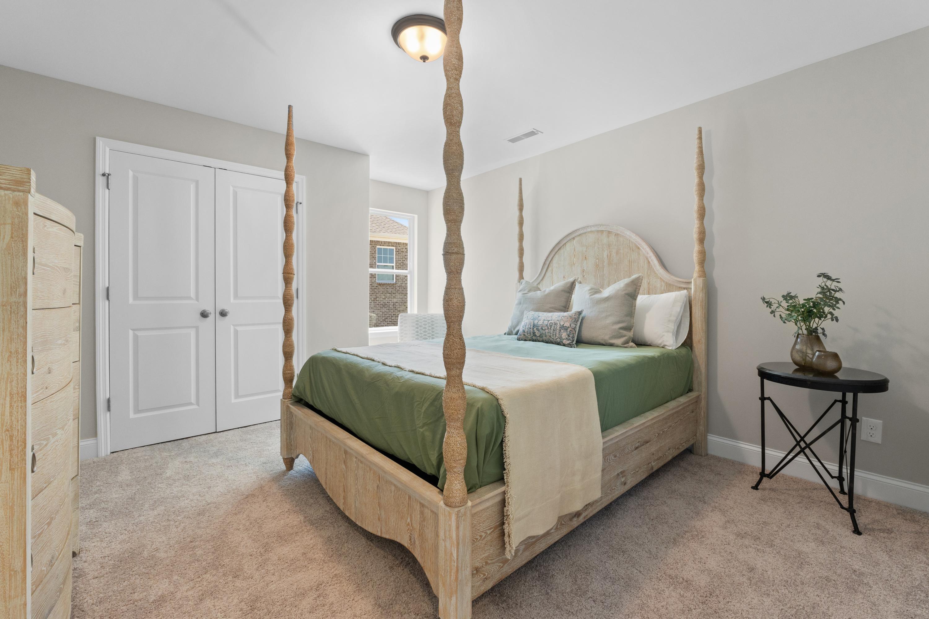 Master bedroom in The Haven D showcasing four-poster bed with green bedding, beige walls, and neutral decor