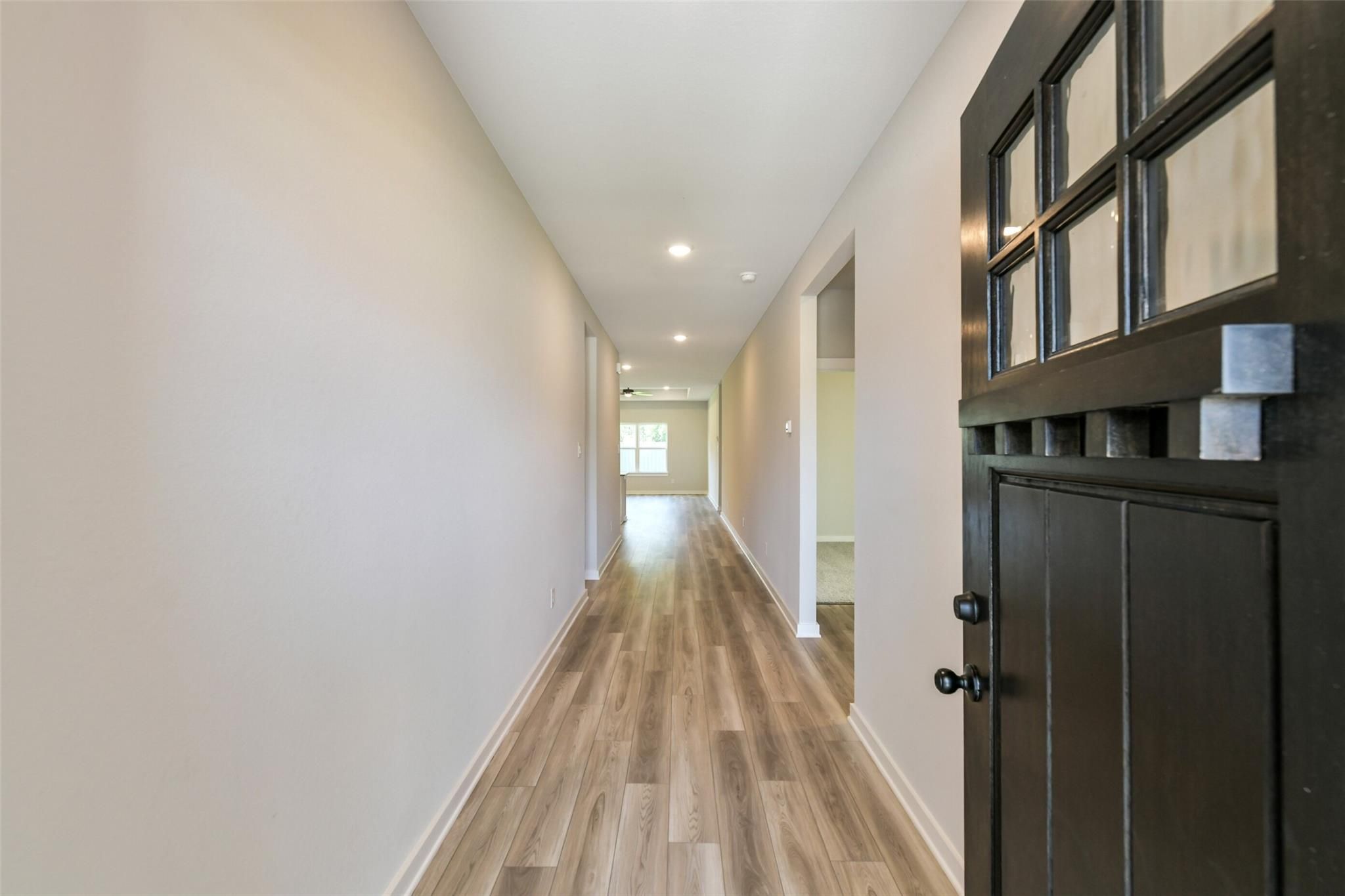 Long hallway with luxury vinyl plank flooring, neutral walls, and recessed lights to front door in Davidson Homes The Daphne H, Crosby Texas