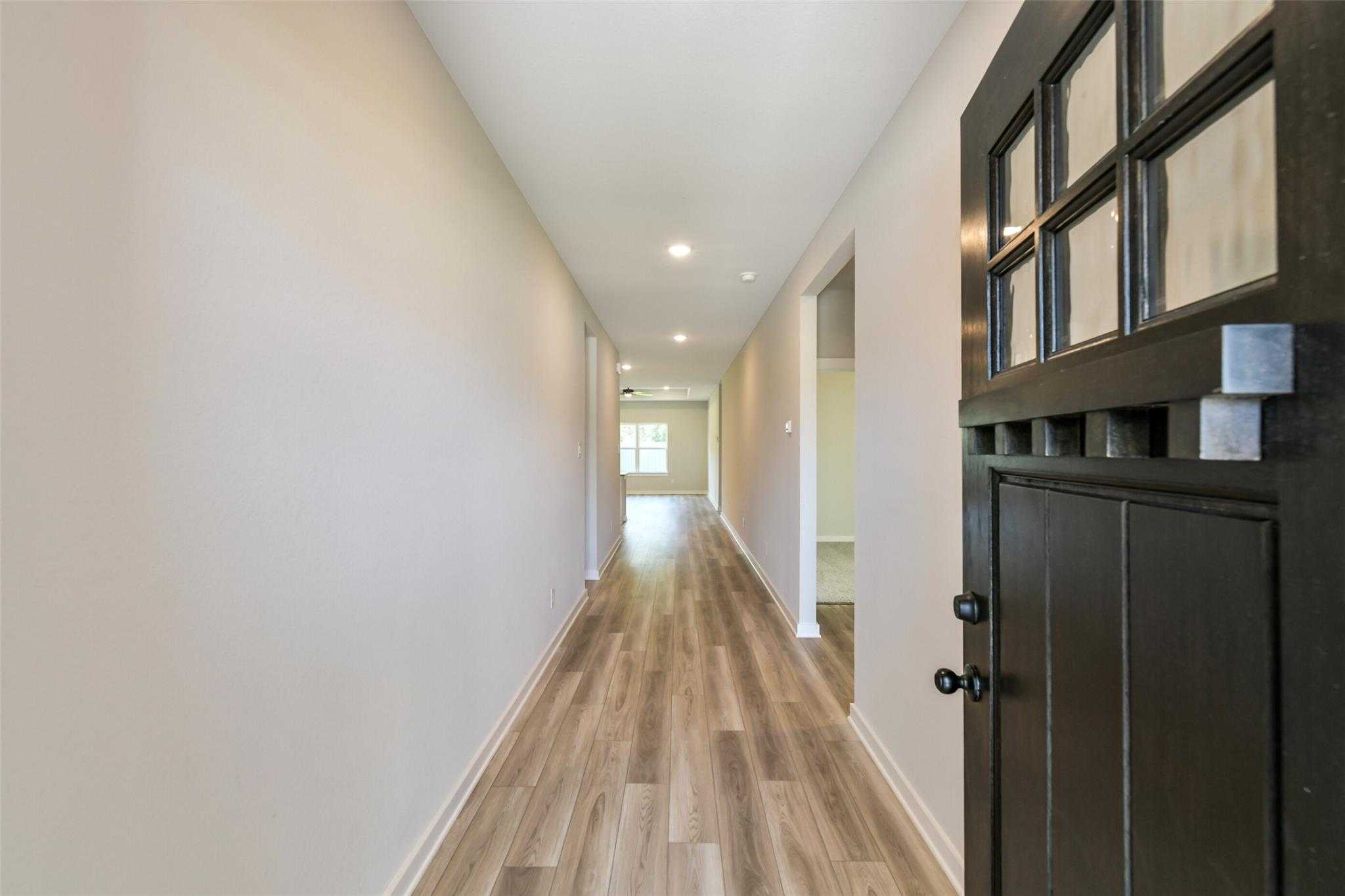 Long hallway with luxury vinyl plank flooring, neutral walls, and recessed lights to front door in Davidson Homes The Daphne H, Crosby Texas