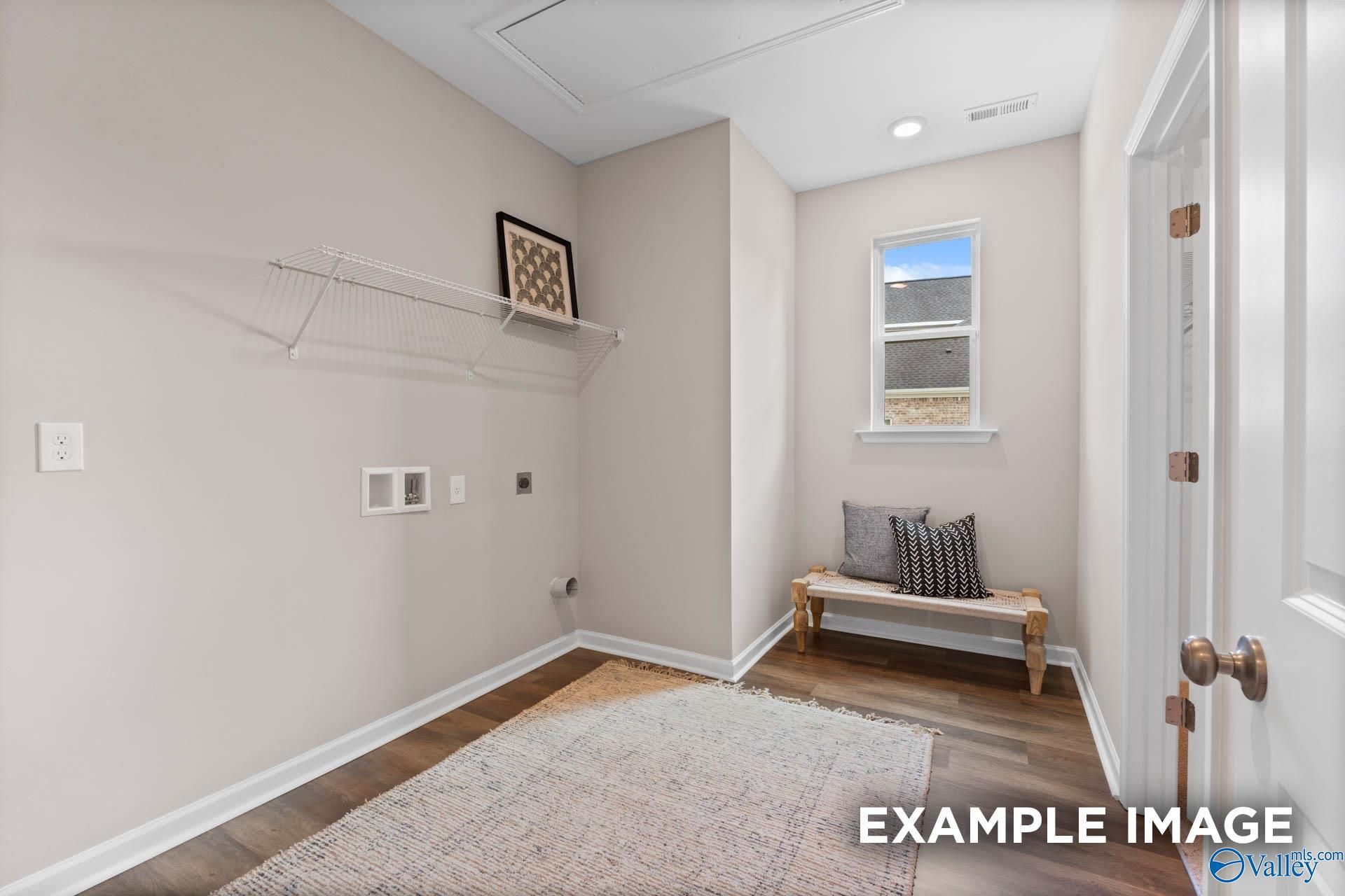 Cozy laundry room featuring built-in shelves, cushioned bench seat, window, and hardwood floors in Evermore Homes The Arcadia M, Owens Cross Roads, Alabama