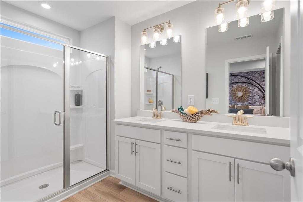 Modern master bathroom featuring double white vanity, frameless glass shower, and mirrored sconces in Davidson Homes Wilmington B, Emerson, GA