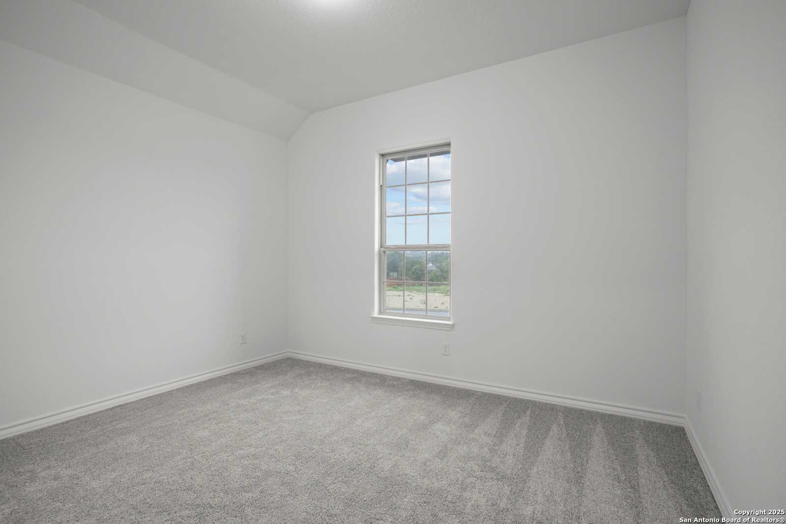 Bright empty secondary bedroom with white walls, gray carpet, and large window view in Davidson Homes The Summerlin B, Castroville, Texas