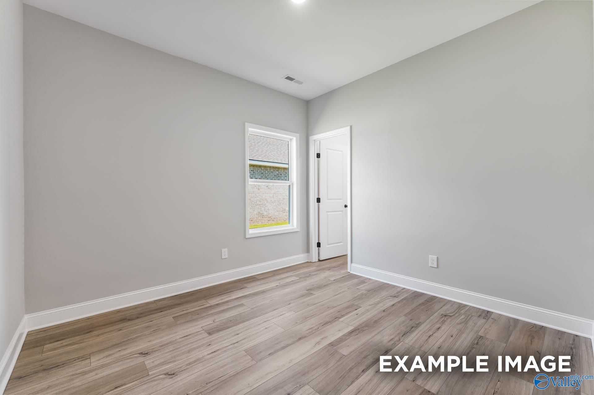 Spacious secondary bedroom with light gray walls, window blinds, and hardwood floors in Davidson Homes The Daphne C, Athens AL
