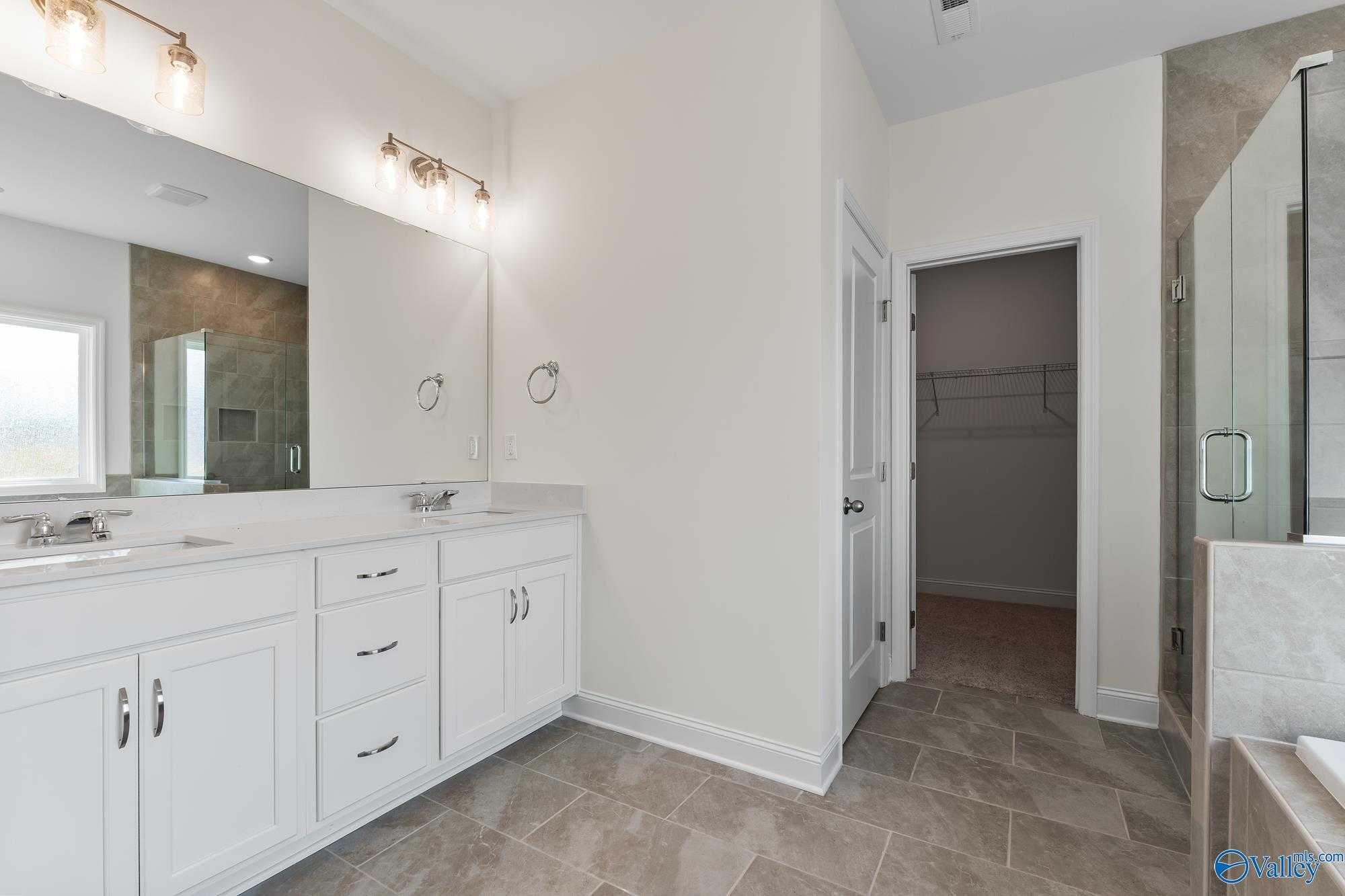 Elegant master bathroom with double vanity, frameless glass shower, and adjacent closet in Davidson Homes The Harrison, Meridianville, AL