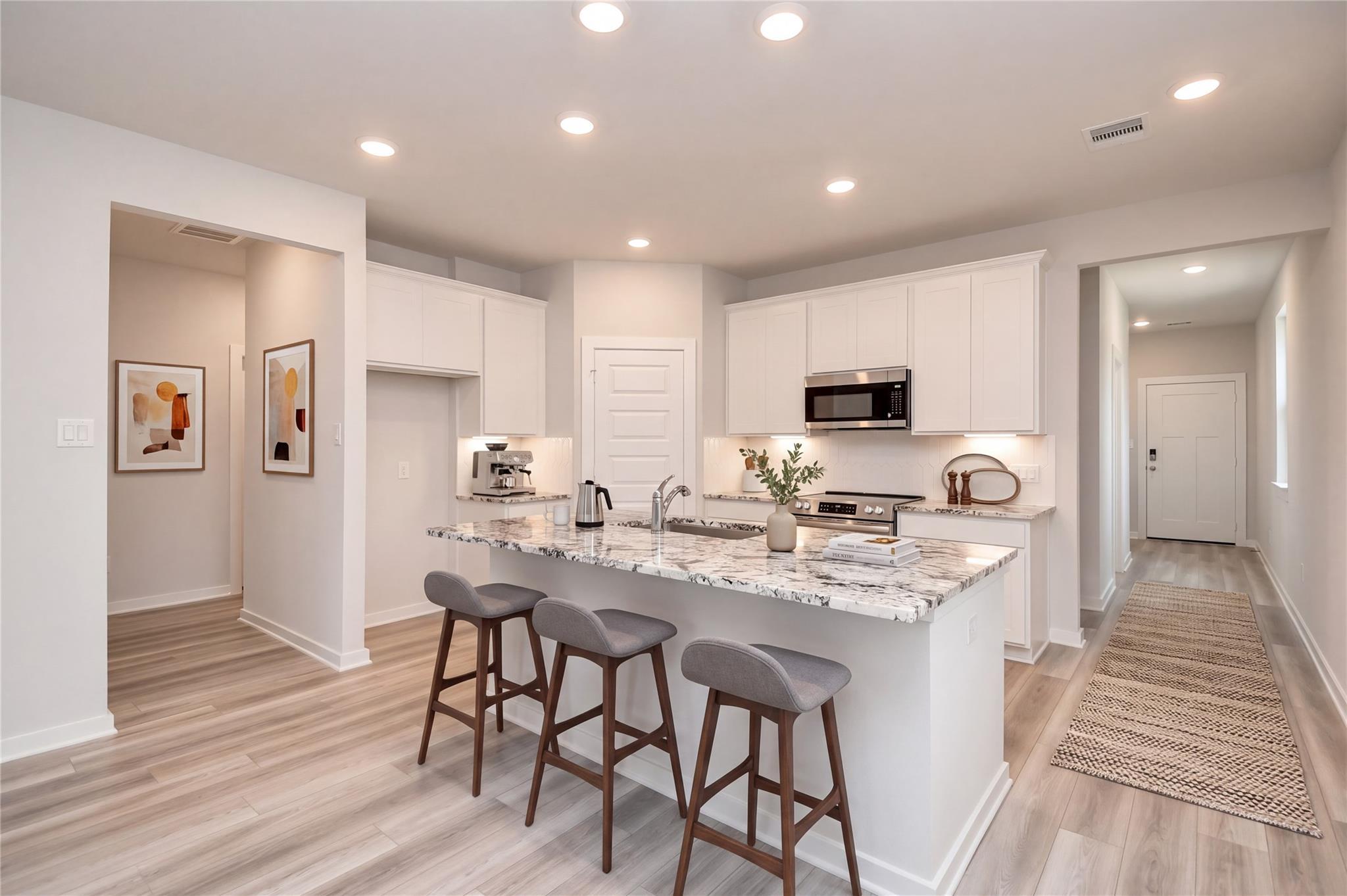 White shaker kitchen with granite island, bar seating, and stainless appliances in Davidson Homes Sabine F plan, Cleveland, TX