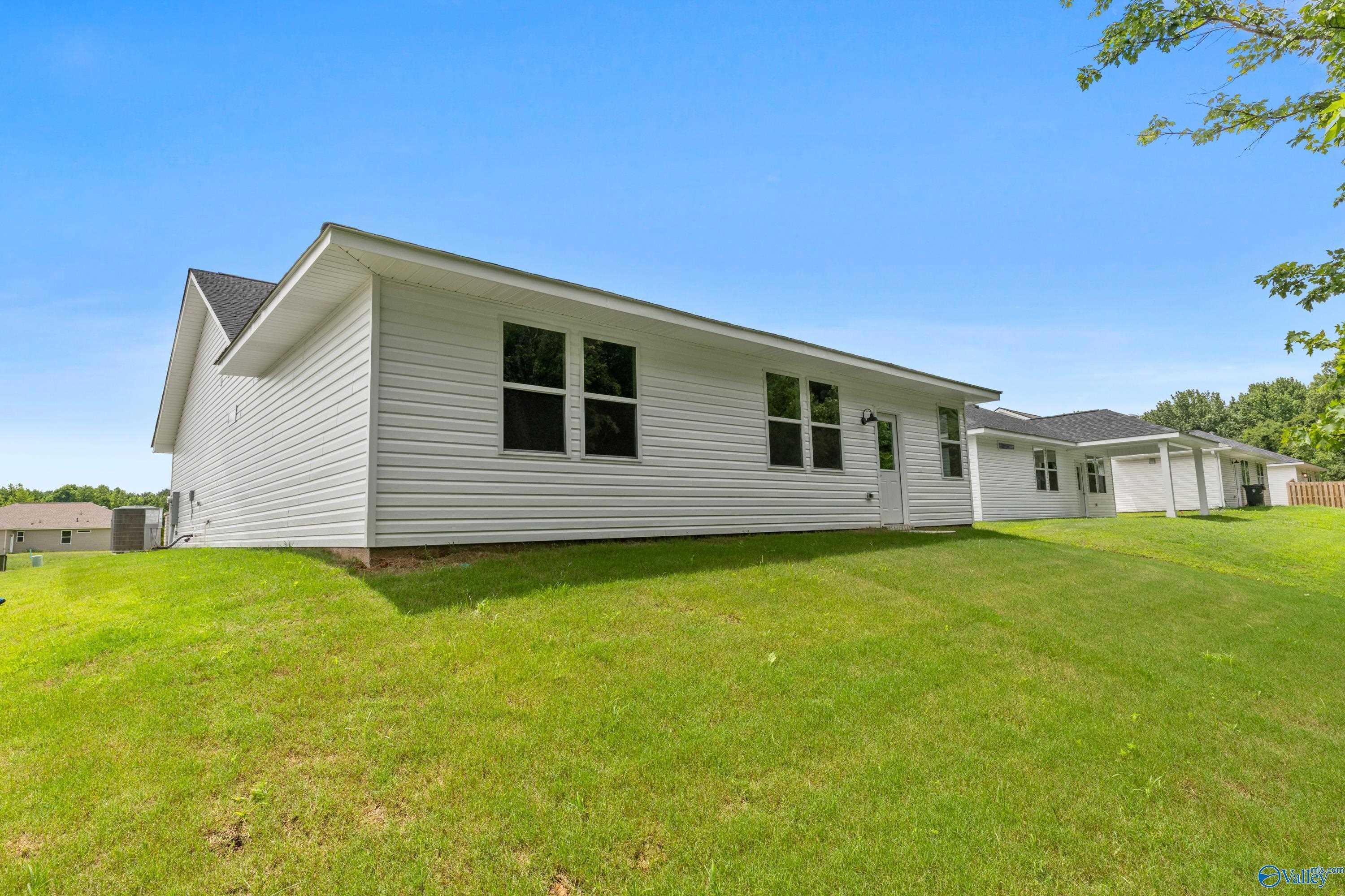 White single-story 3-bedroom home side view with windows and attached garage on green hillside lawn, Forest Glen, Hazel Green, AL