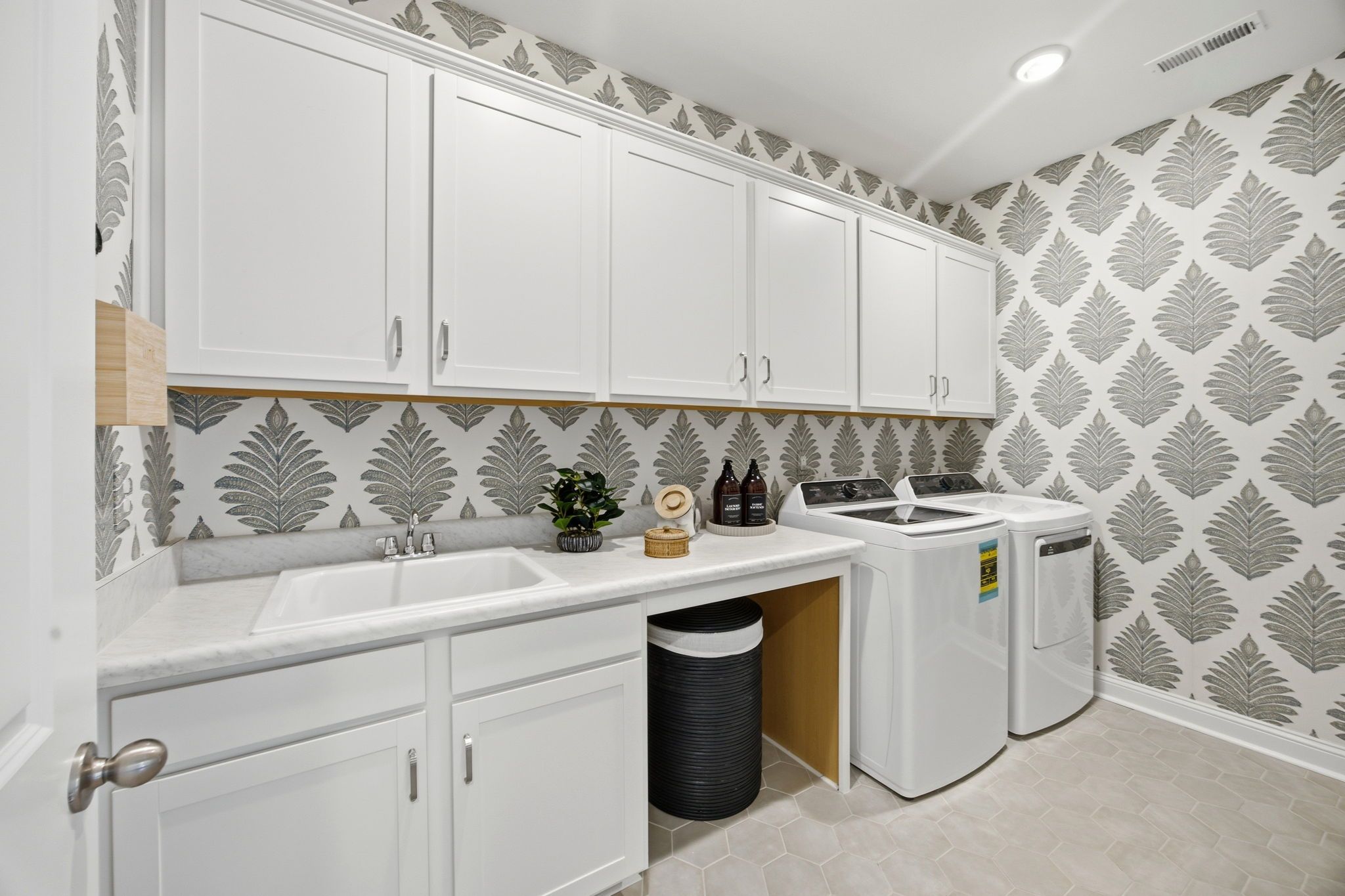 Modern laundry room at Enclave at Belmont in Belmont NC with white shaker cabinets, utility sink, washer dryer and leaf wallpaper