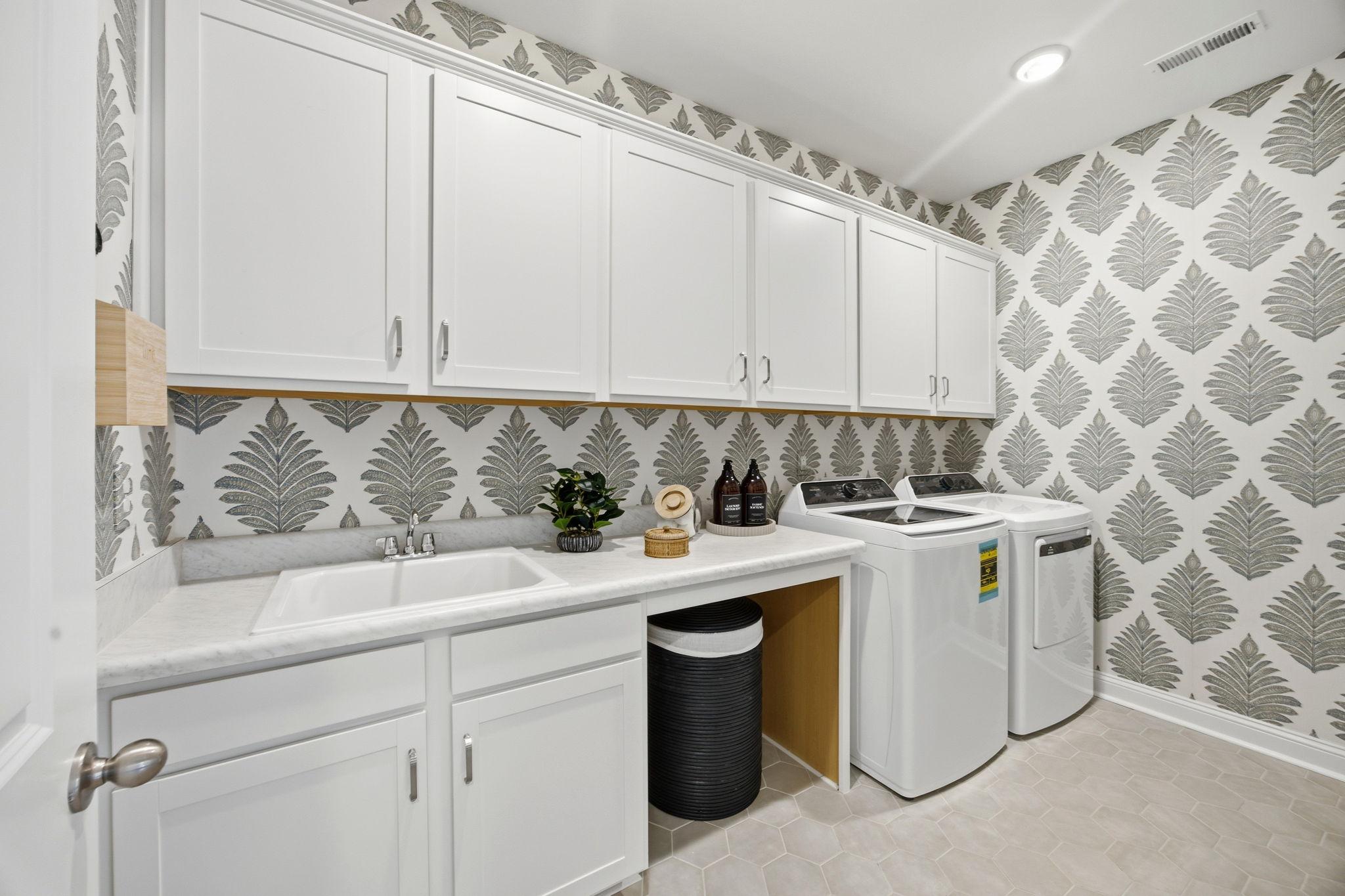 Modern laundry room at Enclave at Belmont in Belmont NC with white shaker cabinets, utility sink, washer dryer and leaf wallpaper