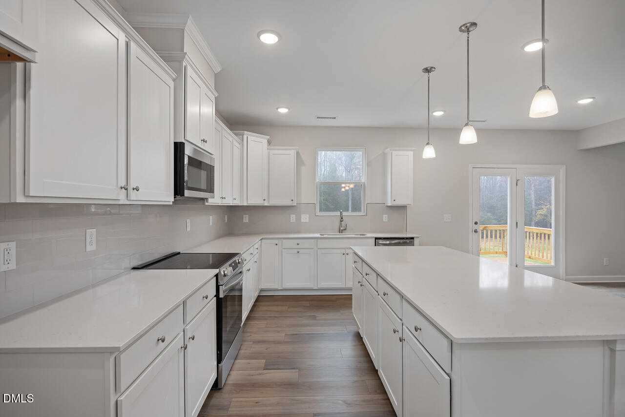 Modern white shaker kitchen with quartz island, stainless appliances, pendant lights, and French doors to patio in Davidson Homes The Hickory II A, Lillington, NC