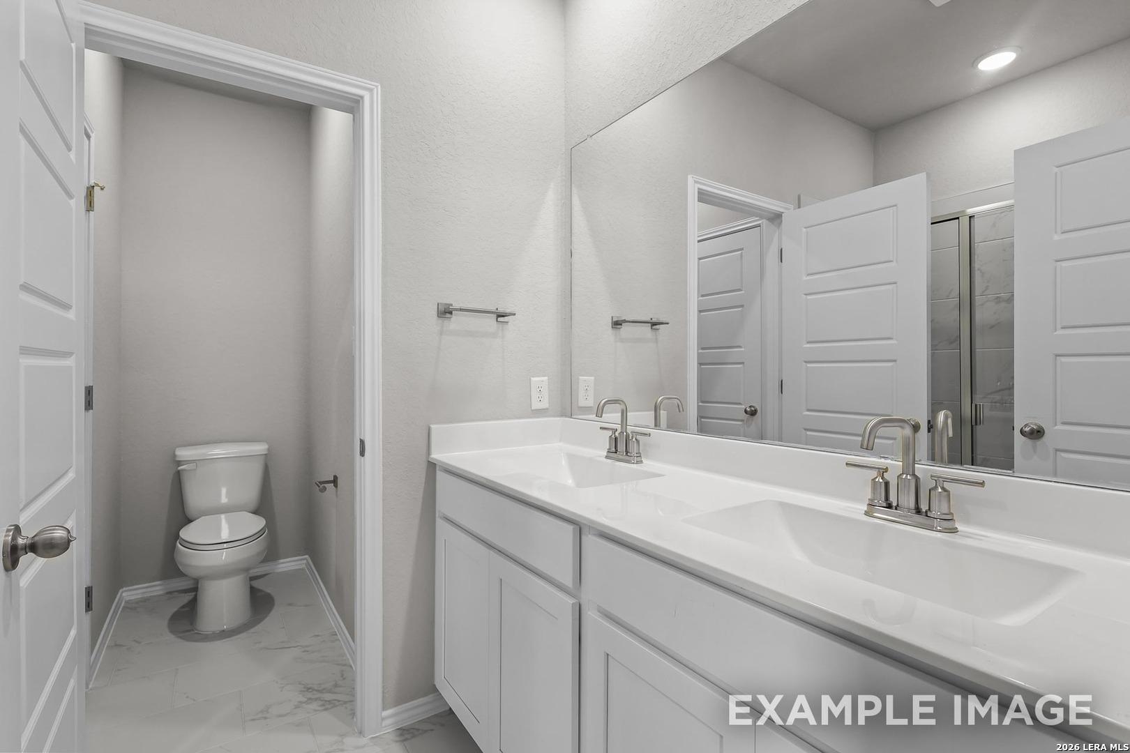Modern master bathroom featuring double white vanity, large mirror, and enclosed toilet in Davidson Homes The Colorado D, San Antonio