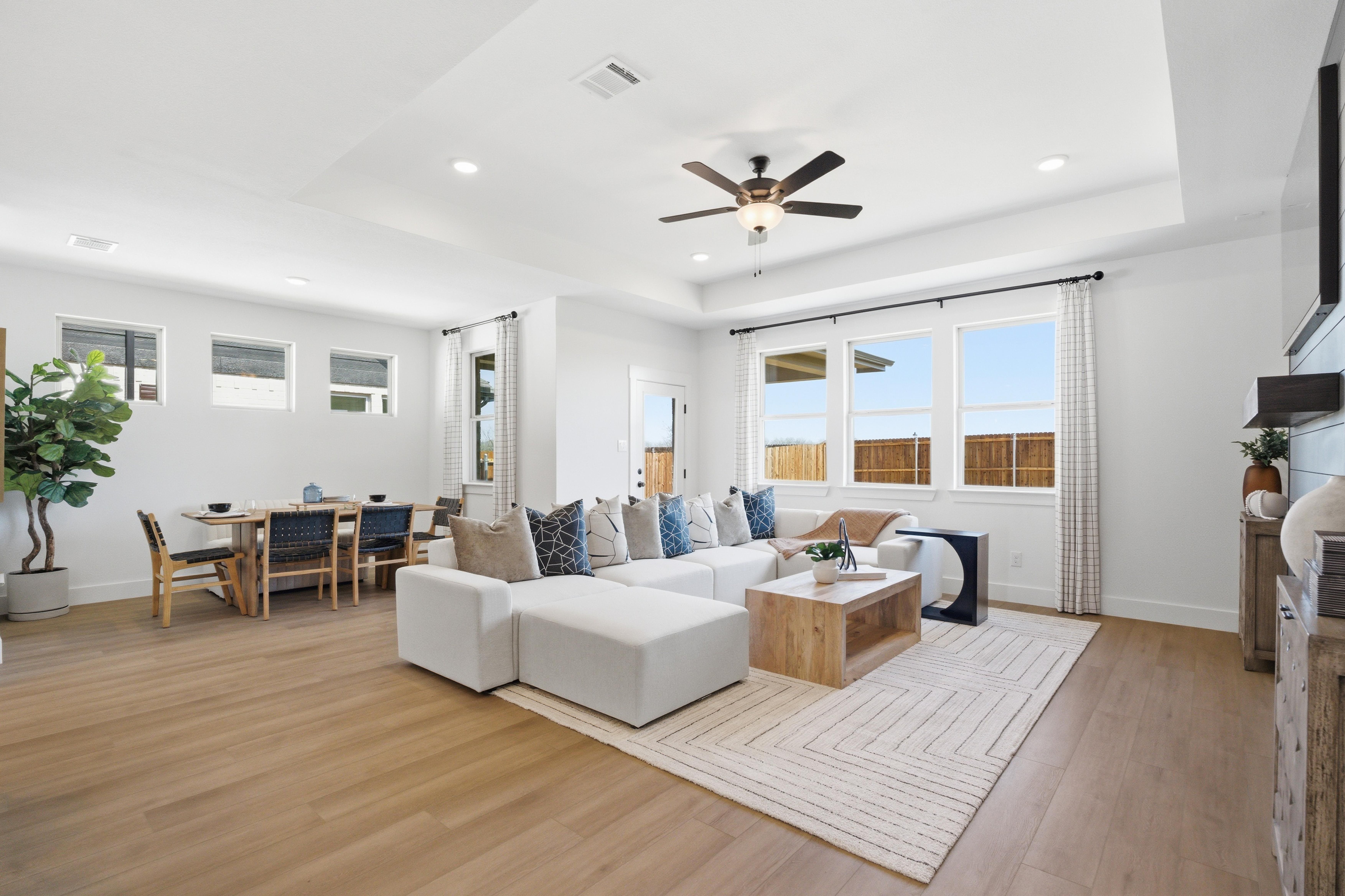 Spacious open-concept living and dining room in Mercer Meadows, Royse City TX with light oak floors, white L-shaped sofa, ceiling fan, and large windows