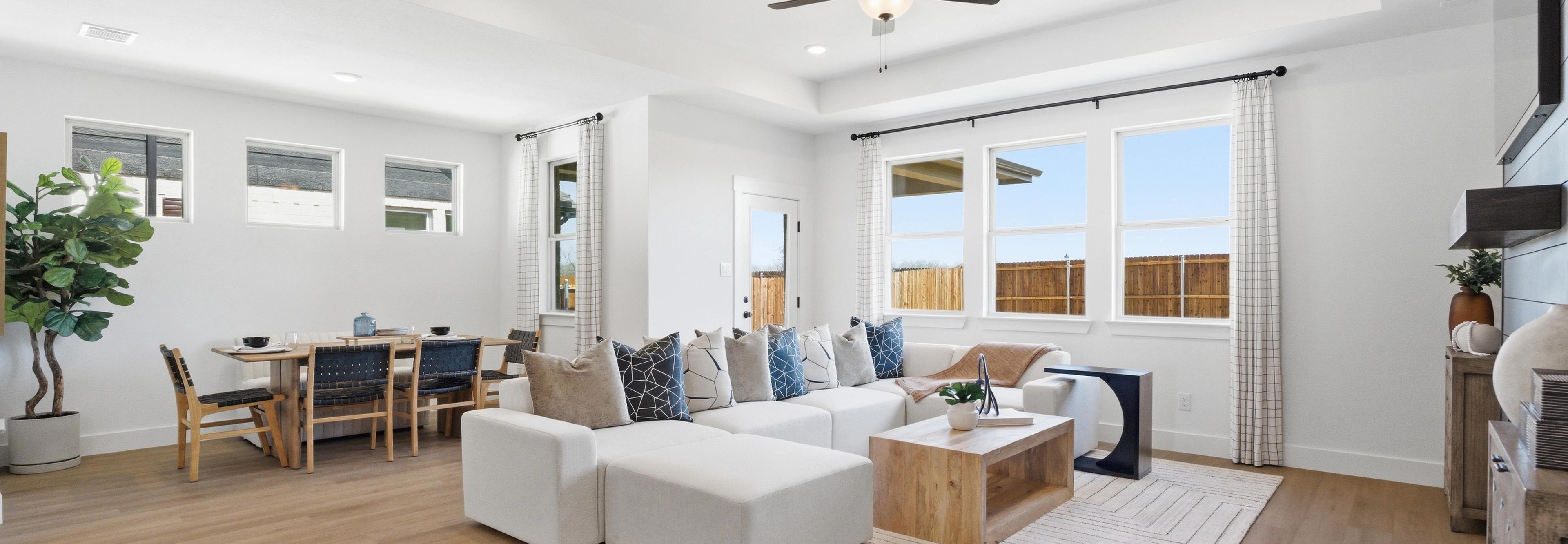 Spacious open-concept living and dining room in Mercer Meadows, Royse City TX with light oak floors, white L-shaped sofa, ceiling fan, and large windows