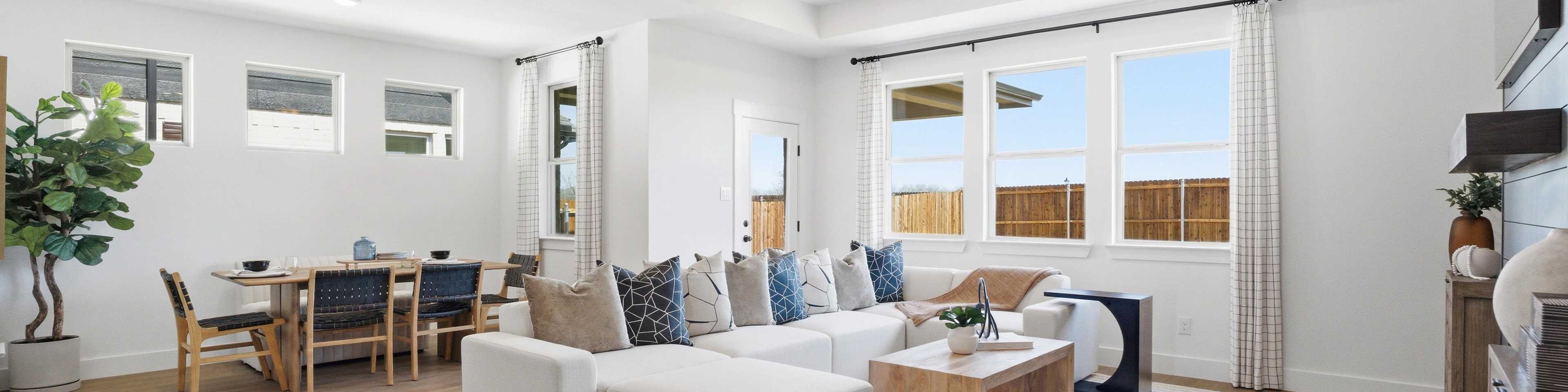 Spacious open-concept living and dining room in Mercer Meadows, Royse City TX with light oak floors, white L-shaped sofa, ceiling fan, and large windows