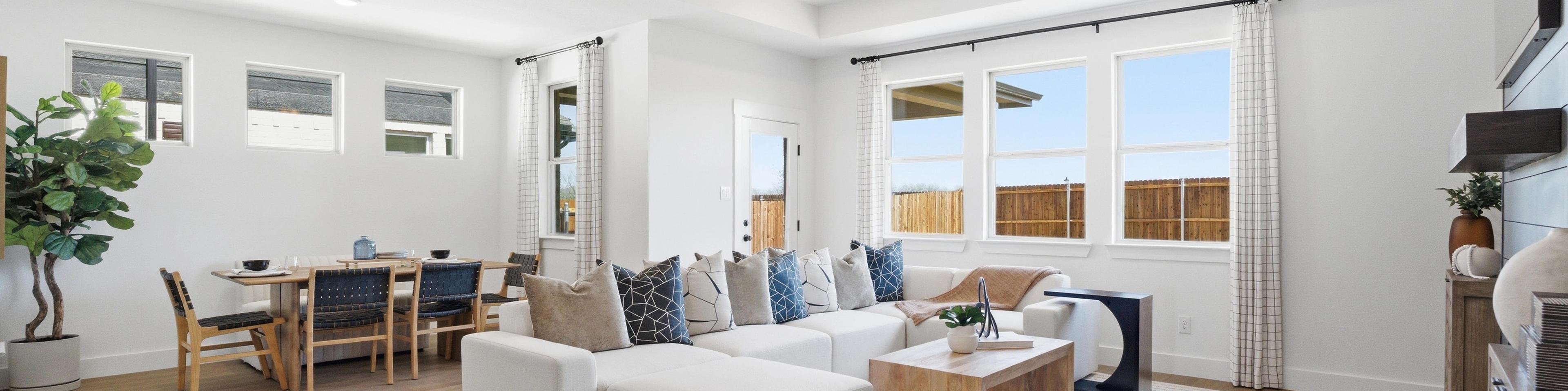 Spacious open-concept living and dining room in Mercer Meadows, Royse City TX with light oak floors, white L-shaped sofa, ceiling fan, and large windows