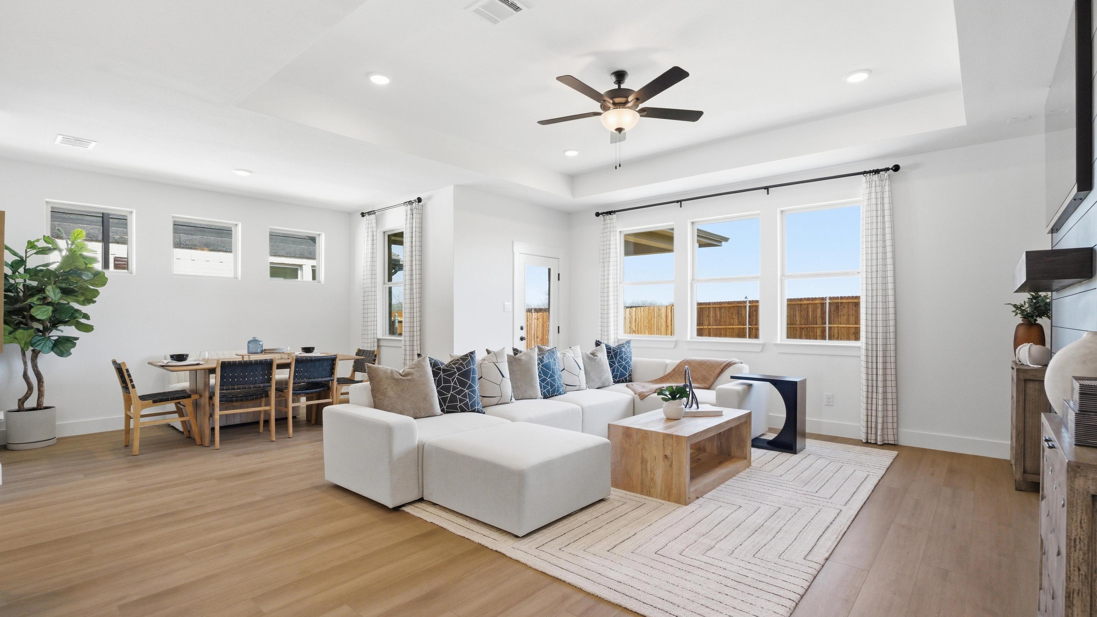 Spacious open-concept living and dining room in Mercer Meadows, Royse City TX with light oak floors, white L-shaped sofa, ceiling fan, and large windows