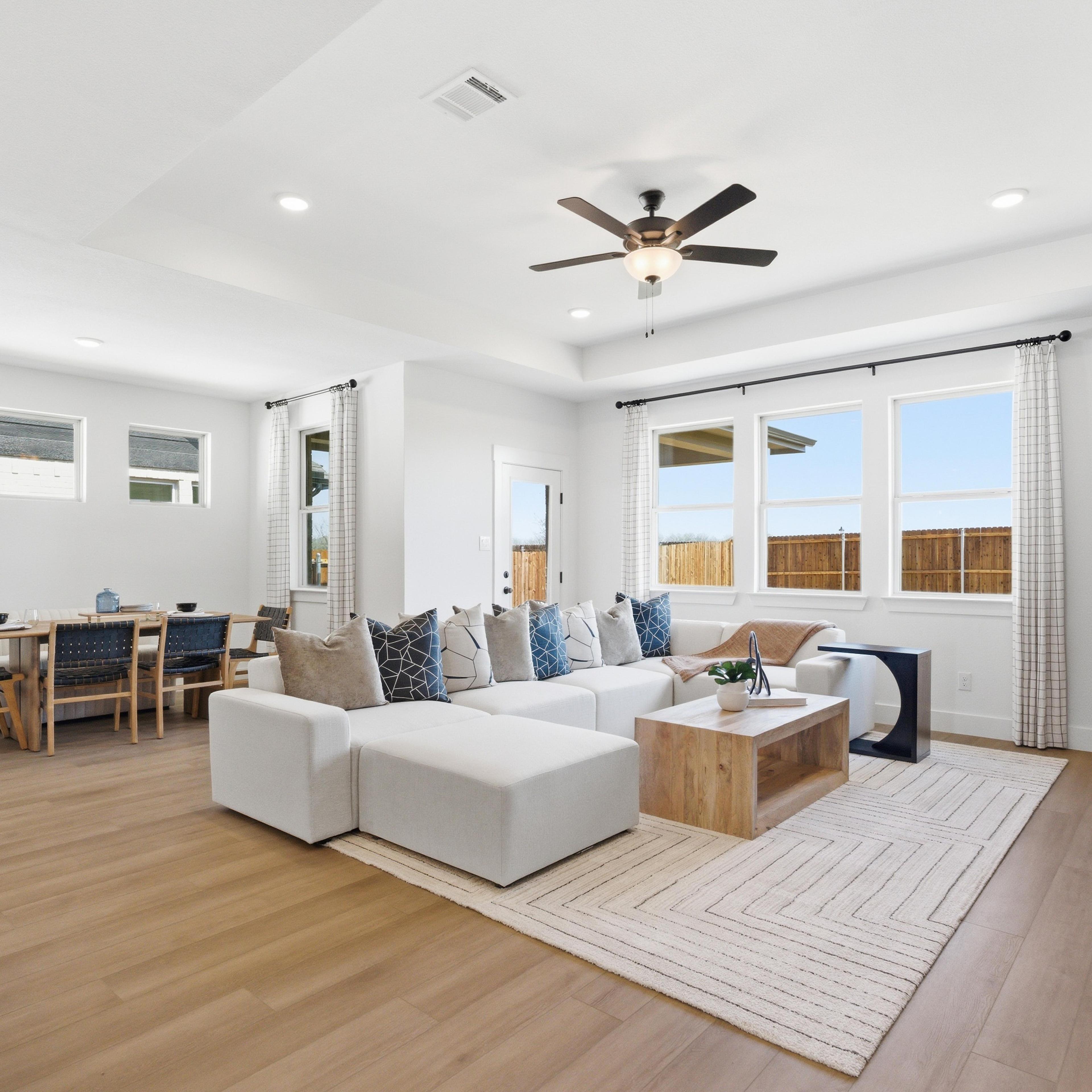 Spacious open-concept living and dining room in Mercer Meadows, Royse City TX with light oak floors, white L-shaped sofa, ceiling fan, and large windows