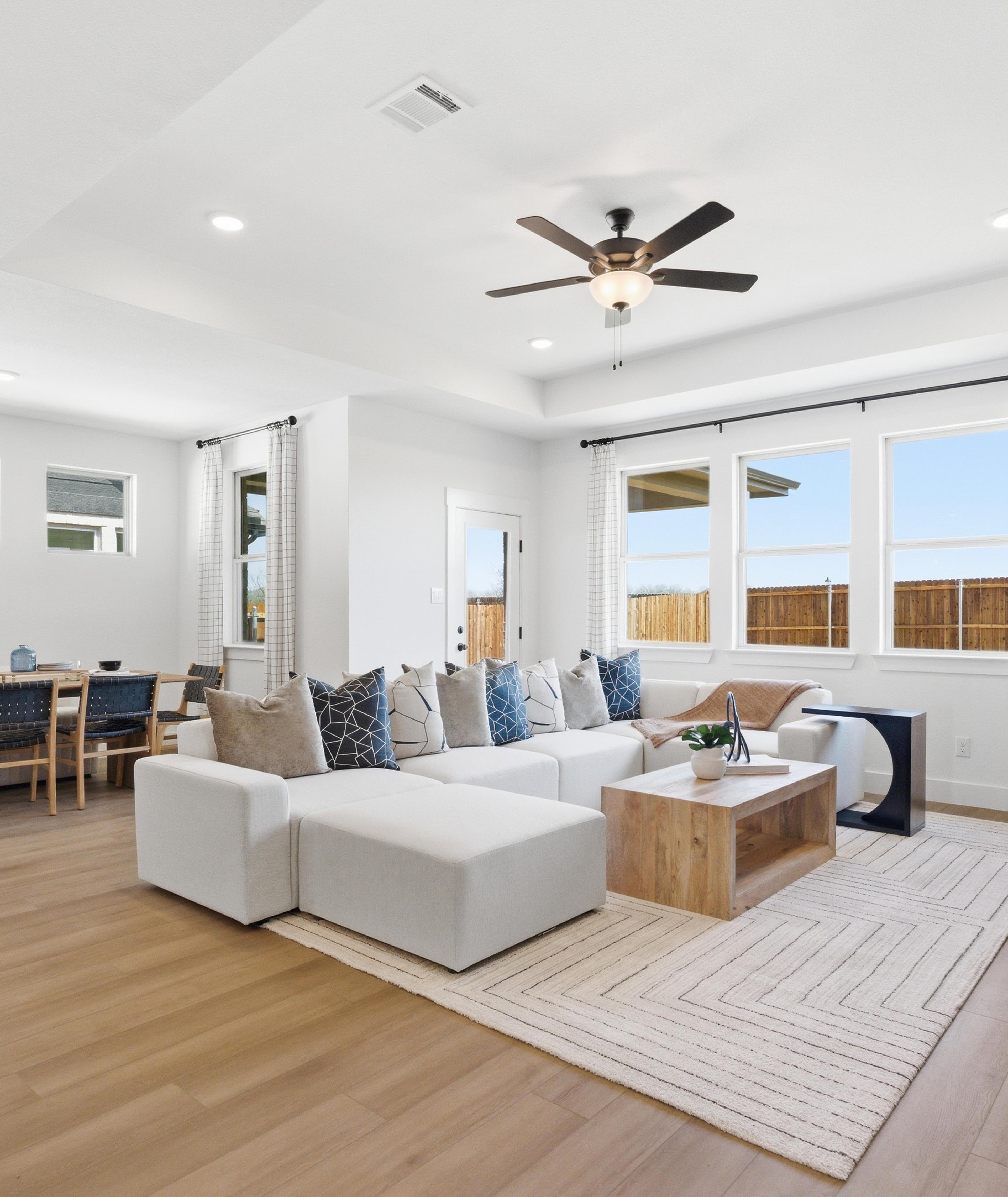 Spacious open-concept living and dining room in Mercer Meadows, Royse City TX with light oak floors, white L-shaped sofa, ceiling fan, and large windows