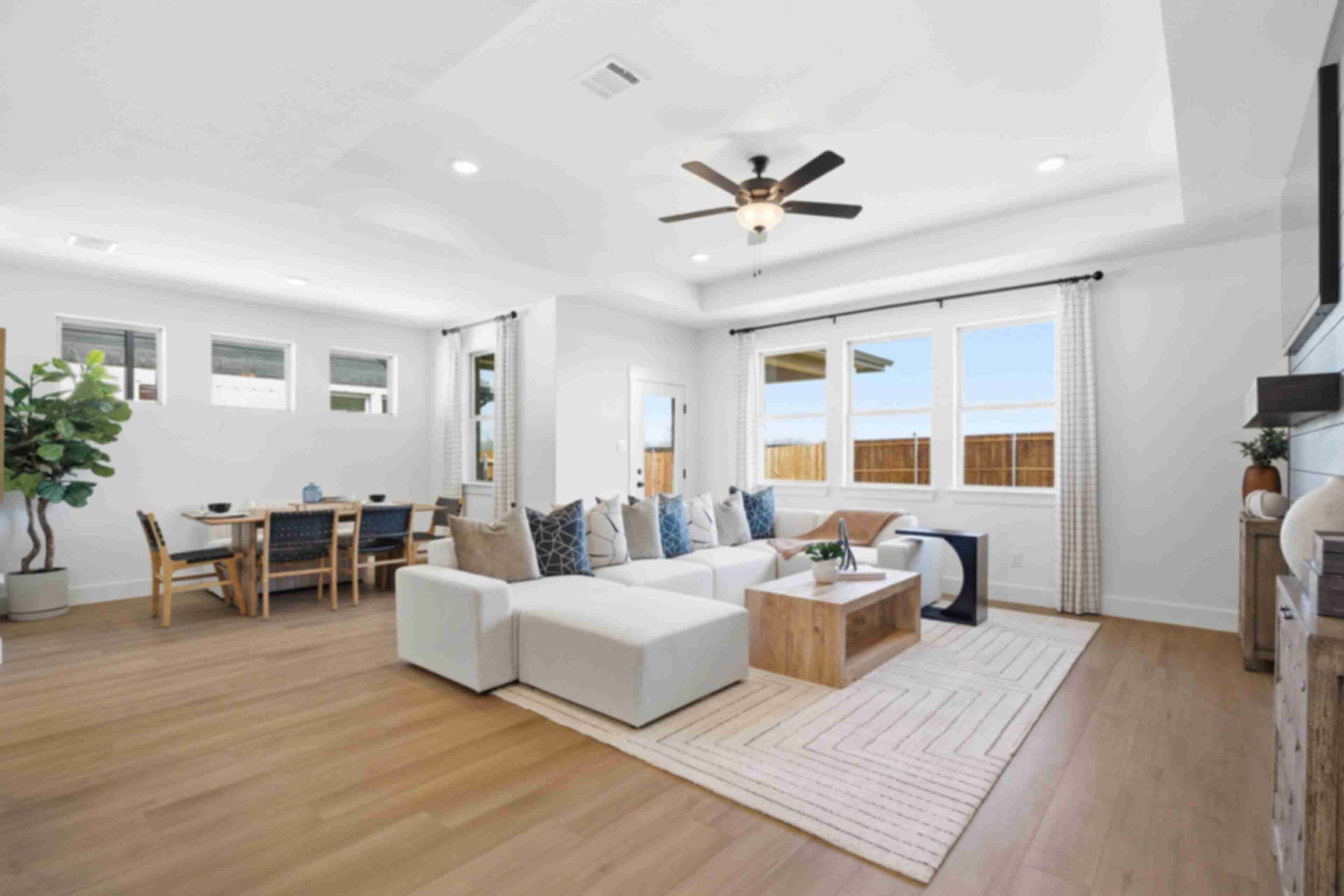 Spacious open-concept living and dining room in Mercer Meadows, Royse City TX with light oak floors, white L-shaped sofa, ceiling fan, and large windows