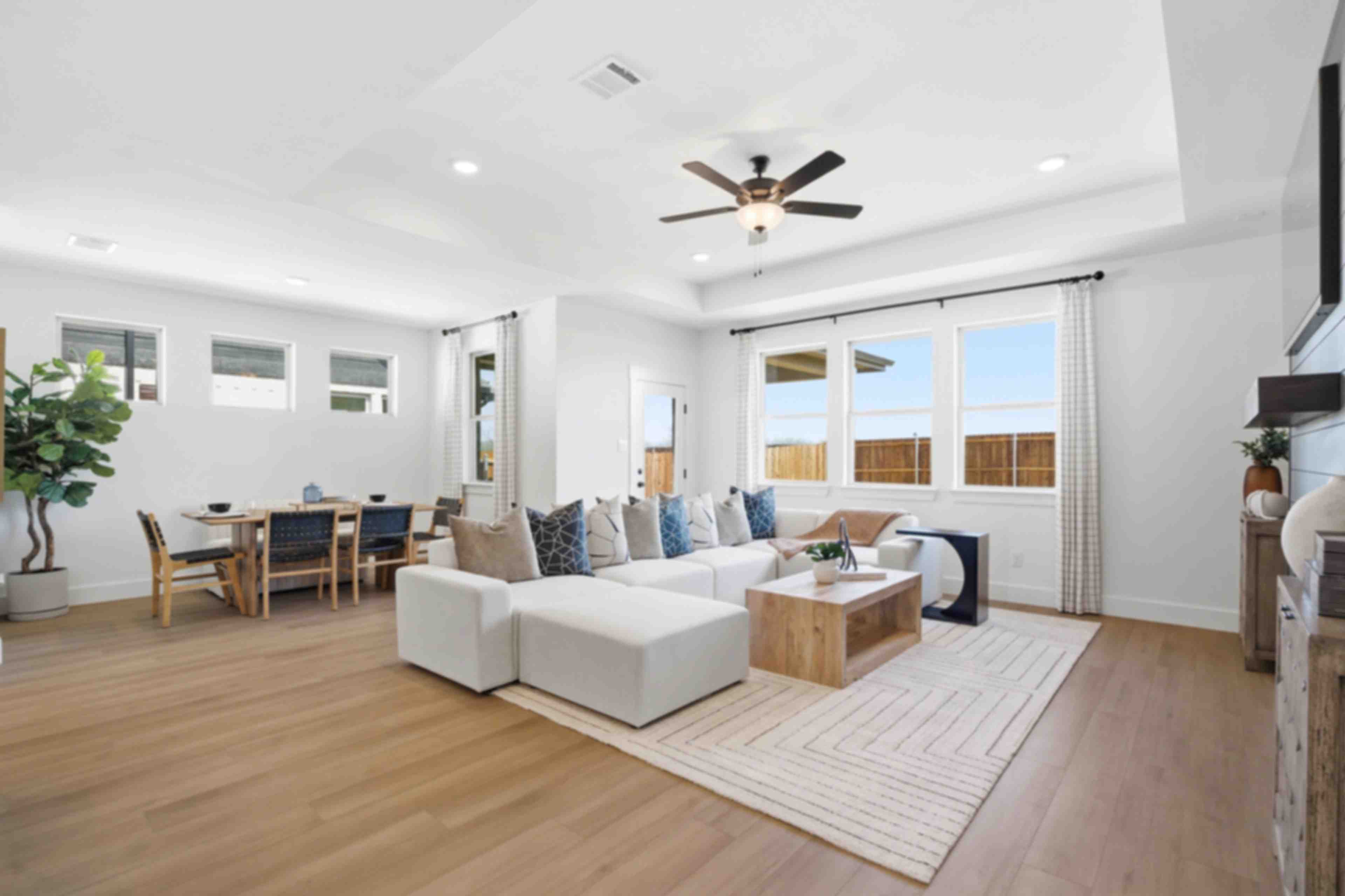 Spacious open-concept living and dining room in Mercer Meadows, Royse City TX with light oak floors, white L-shaped sofa, ceiling fan, and large windows