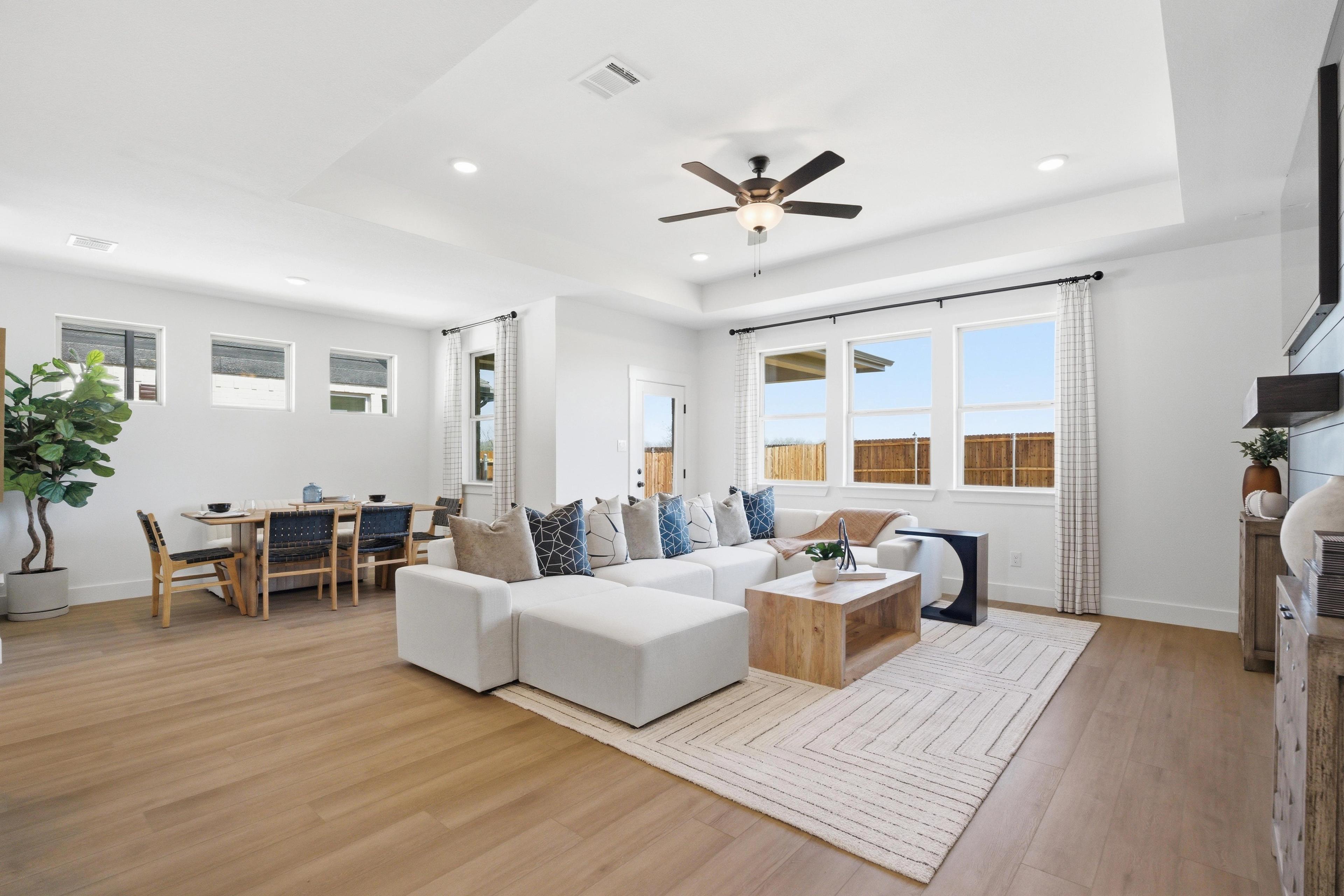 Open-concept living and dining room at Mercer Meadows in Royse City TX with white L-shaped sofa, hardwood floors, and large windows