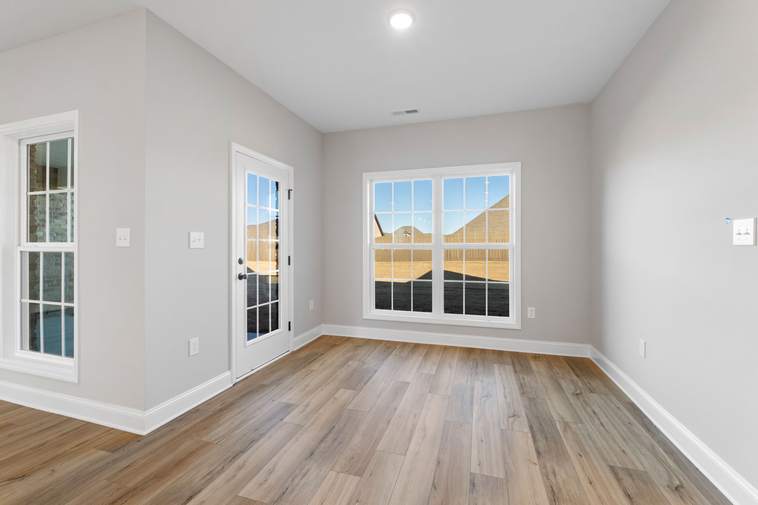 Spacious Valencia home office with light gray walls, hardwood floors, French doors, and large windows overlooking backyard