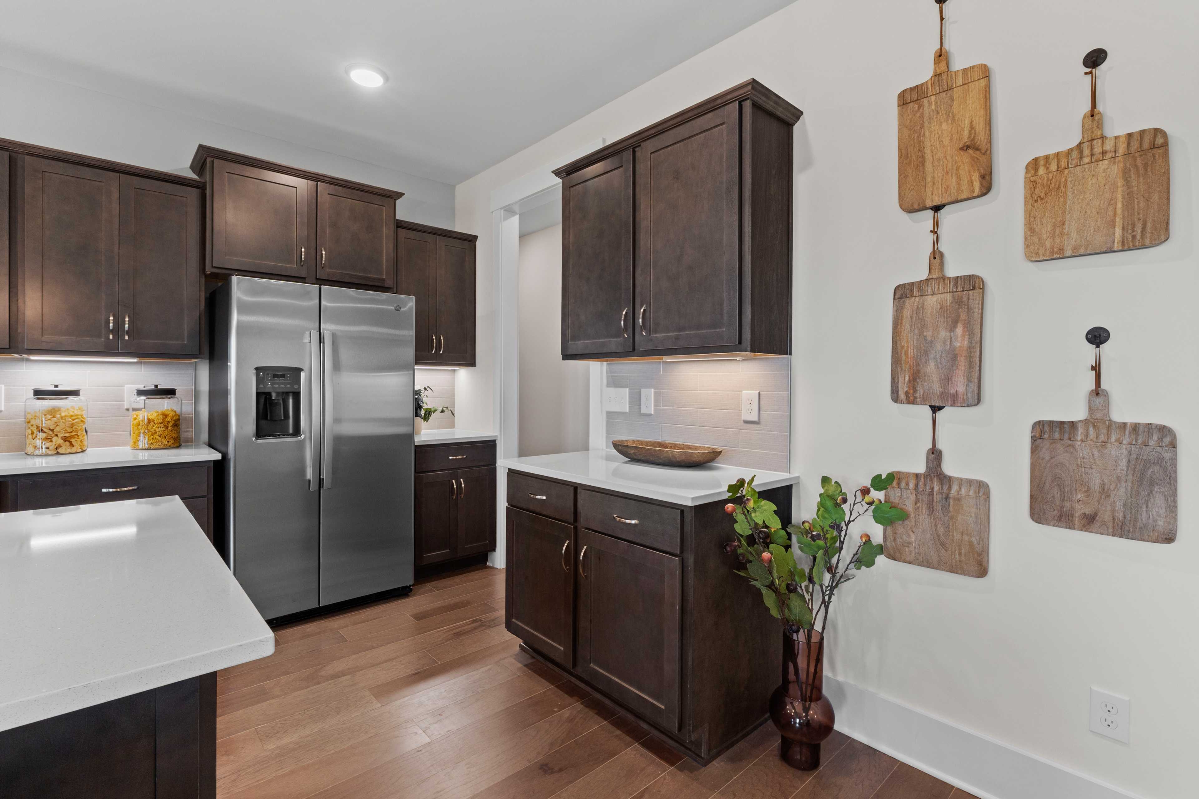 Modern kitchen in Creekside Harvest AL with dark shaker cabinets, stainless steel fridge, white quartz island, hardwood floors