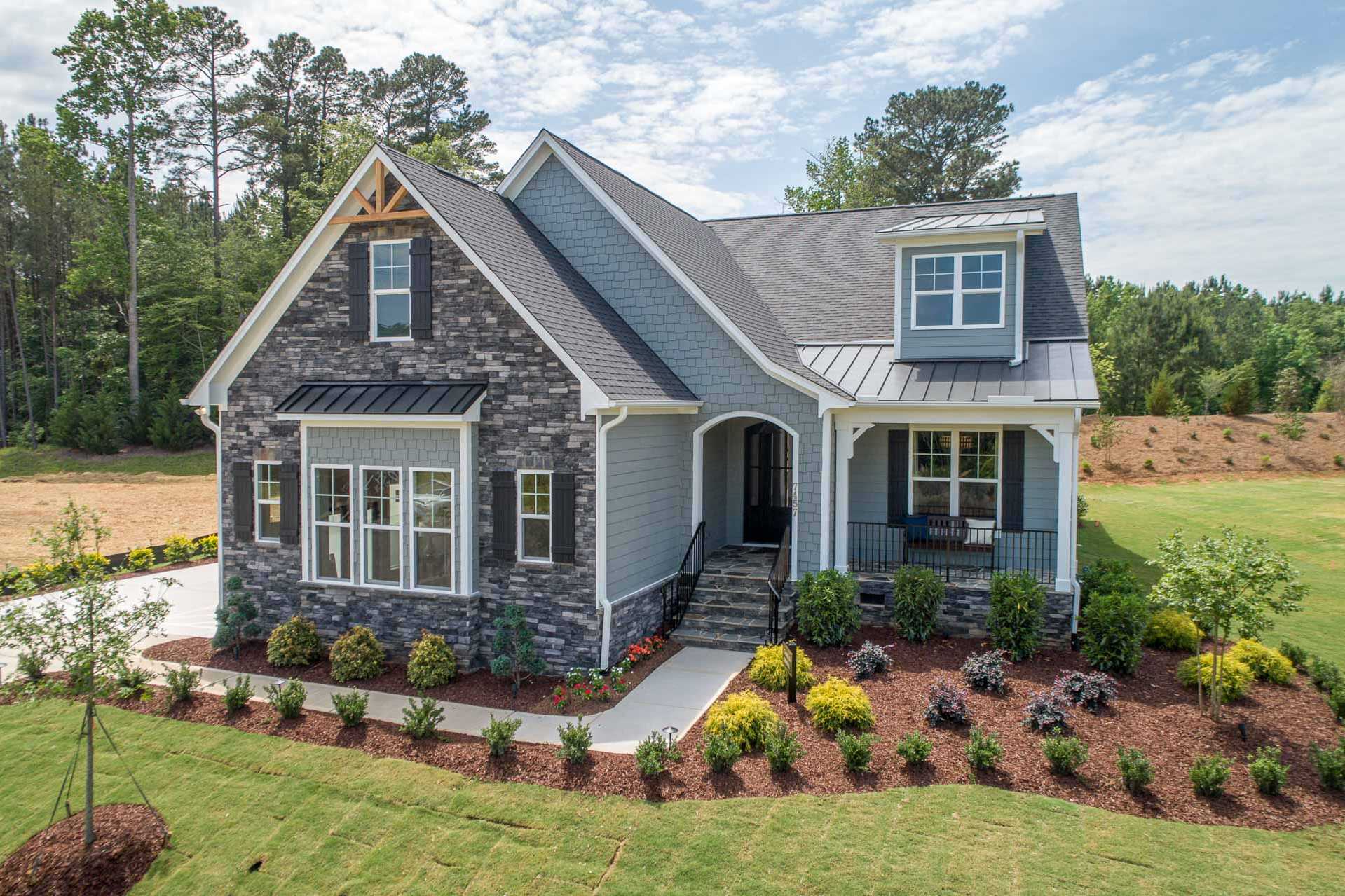 Modern craftsman-style gray home exterior at Hasentree in Wake Forest NC with stone accents, gabled roof, covered porch, and lush landscaping